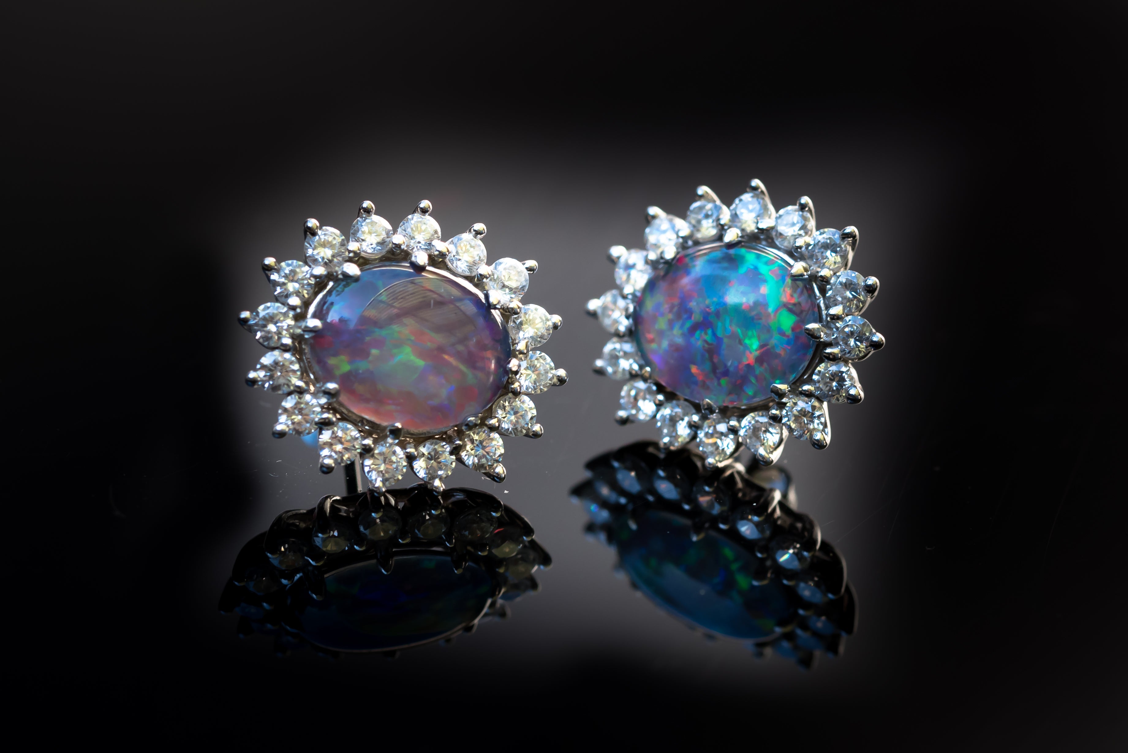 Pair of opal earrings with diamond accents on a black background