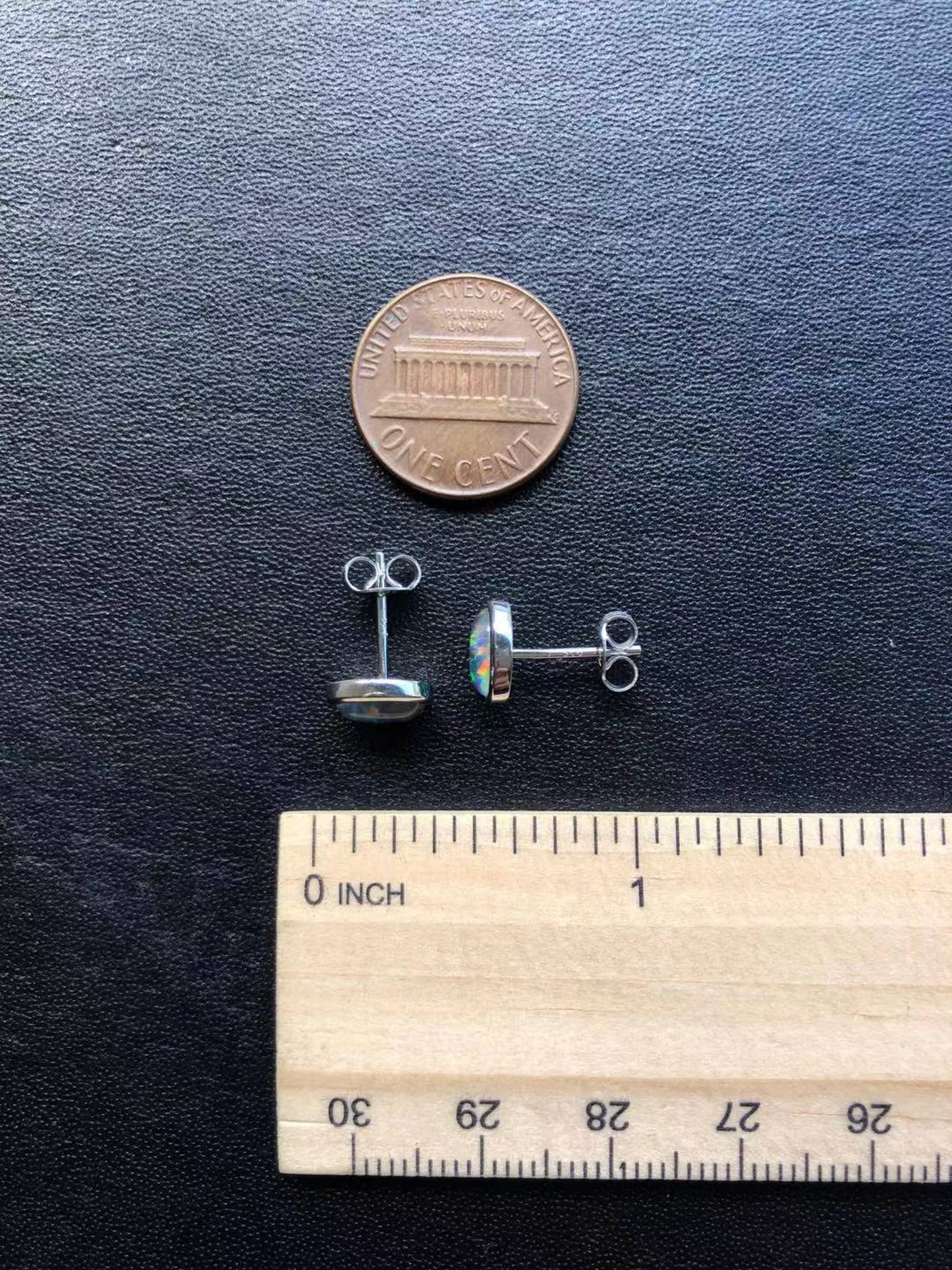 Silver opal earrings on a dark surface with a penny and ruler for scale.