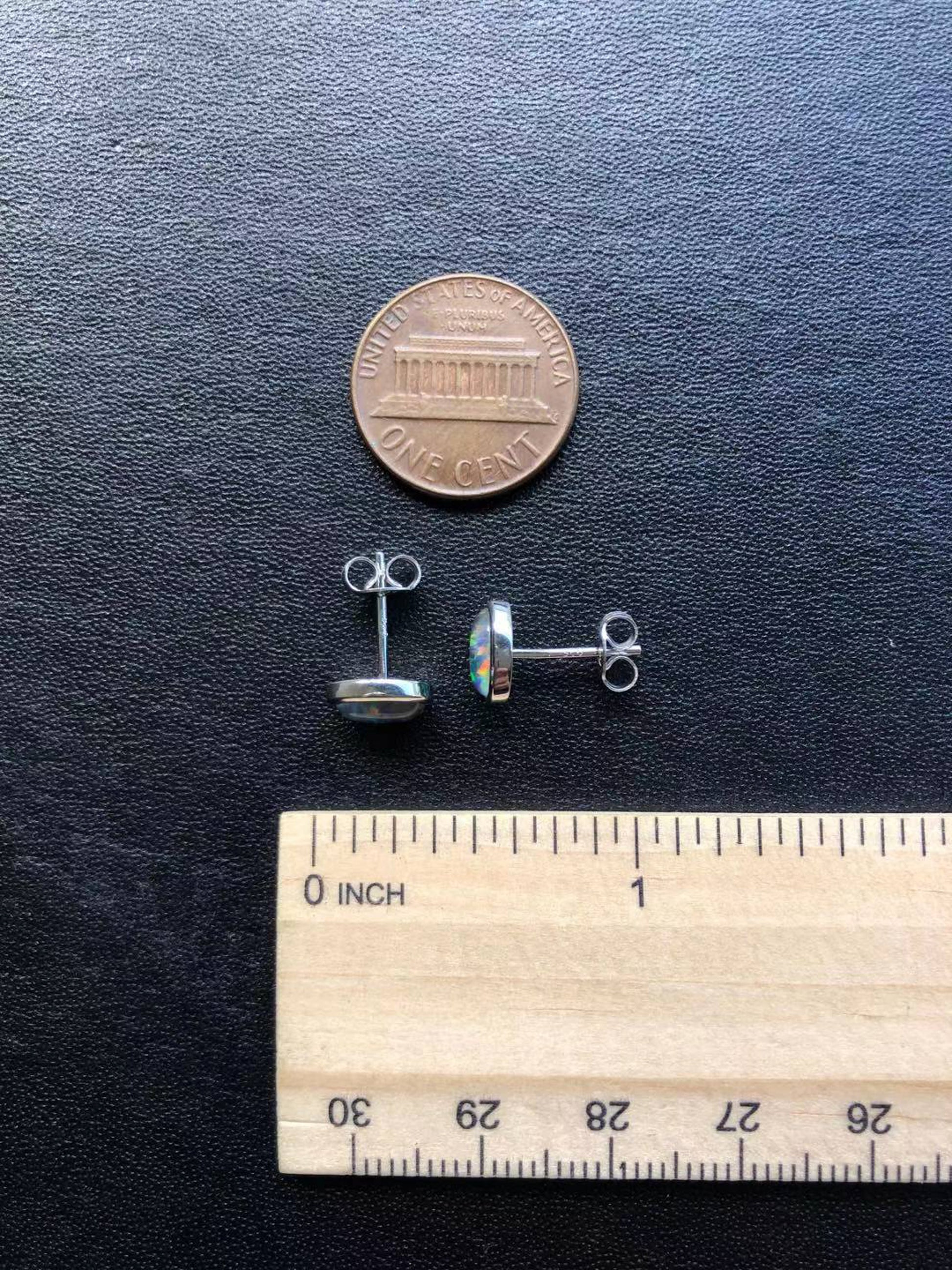 Silver opal earrings on a dark surface with a penny and ruler for scale.
