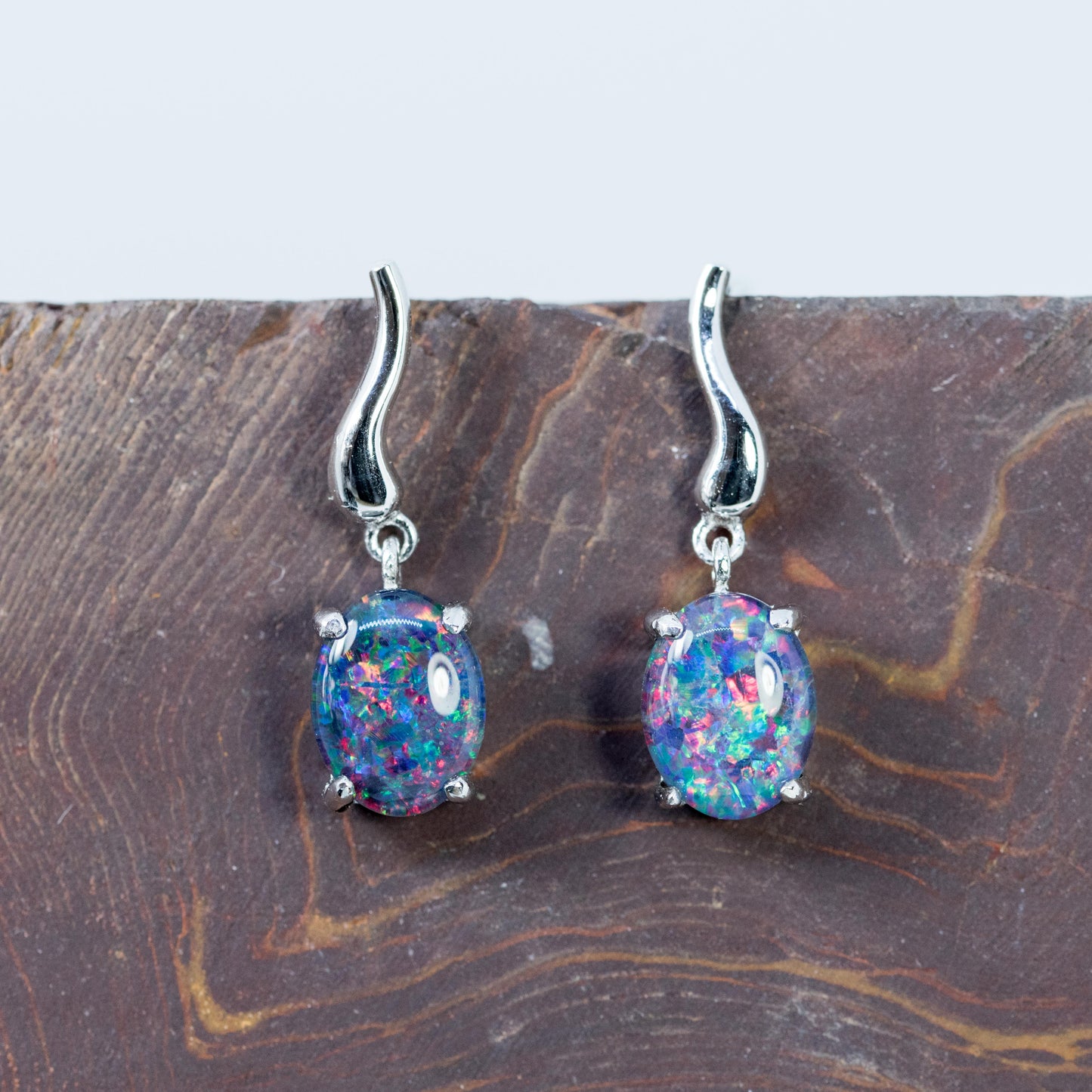 Pair of silver Australian opal earrings with colorful gemstones on a wooden surface