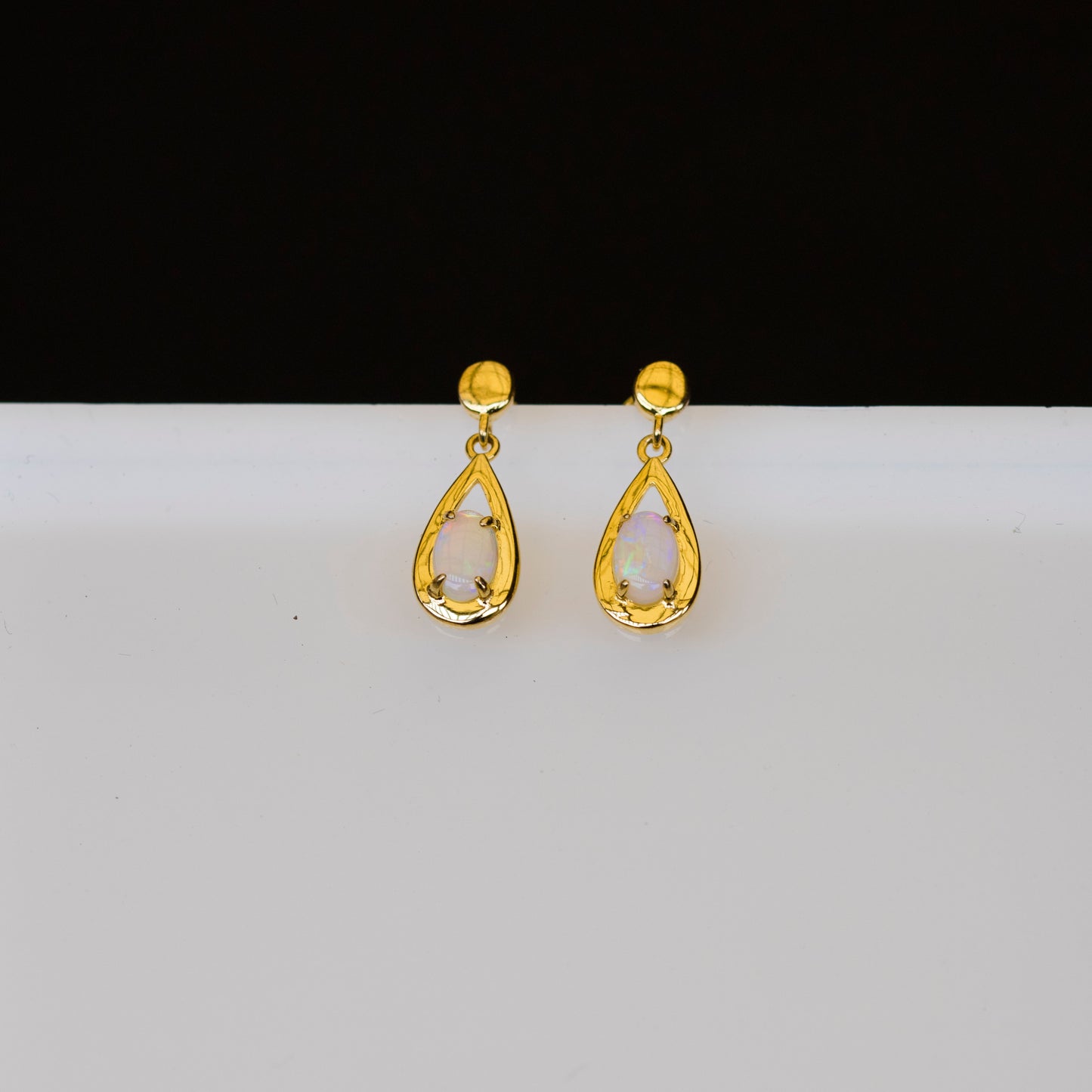 Gold teardrop opal earrings on a white background