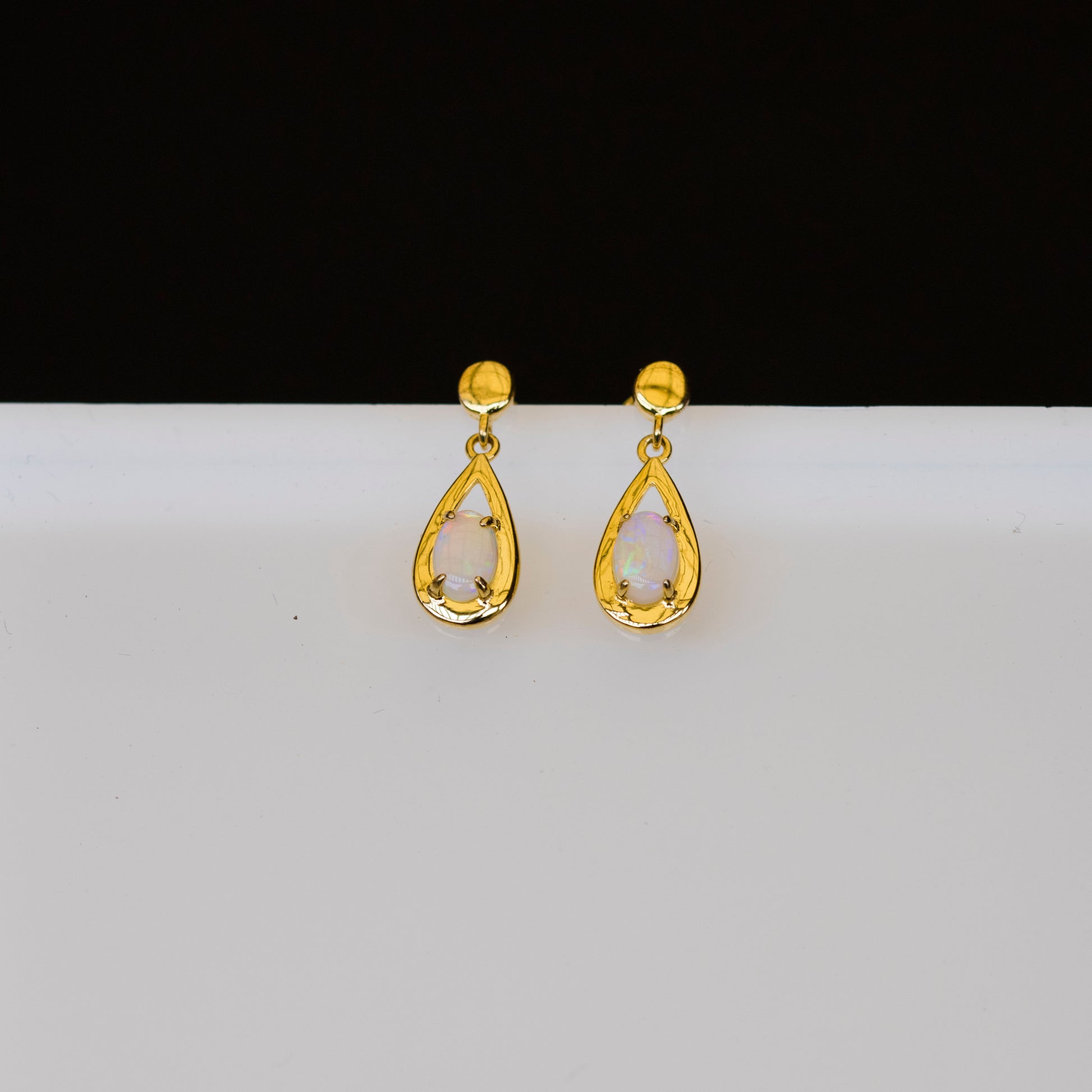 Gold teardrop opal earrings on a white background