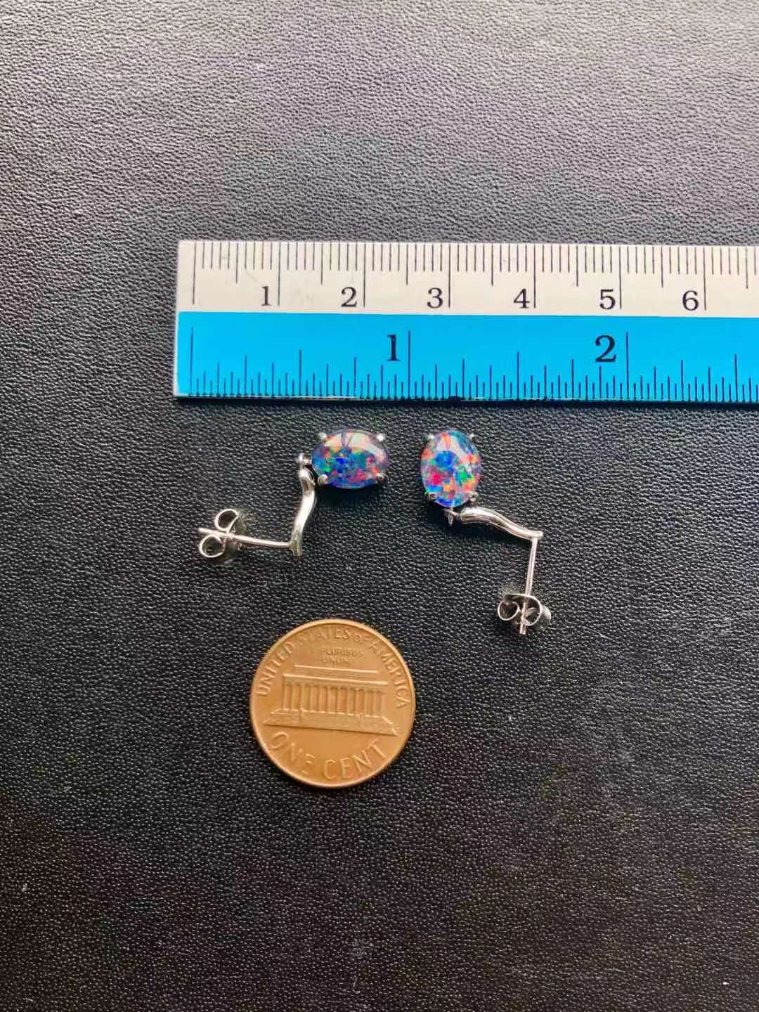 Pair of opal earrings with colorful stones next to a ruler and penny on a black surface