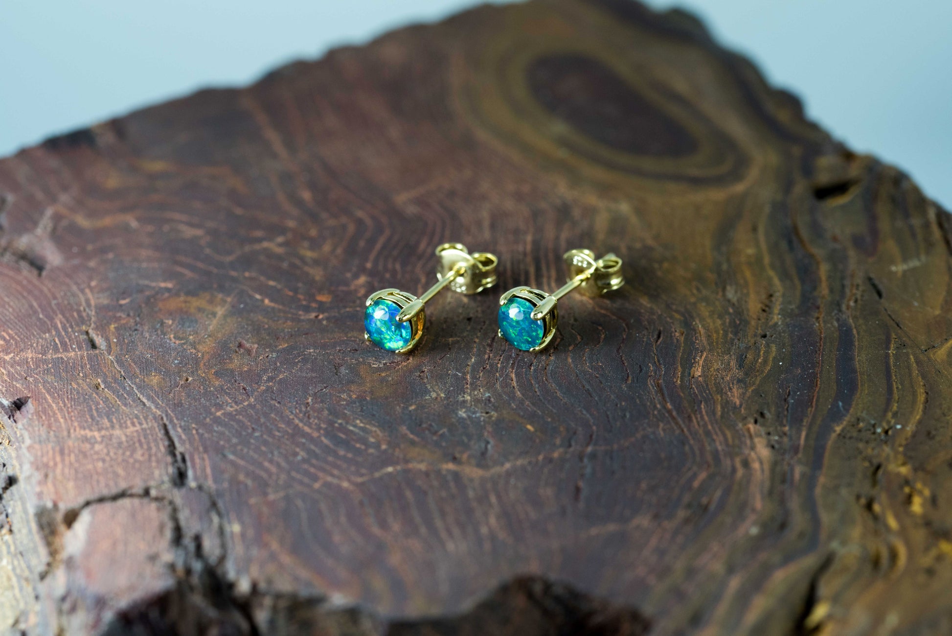 Gold earrings with blue opal gemstones on a wooden surface