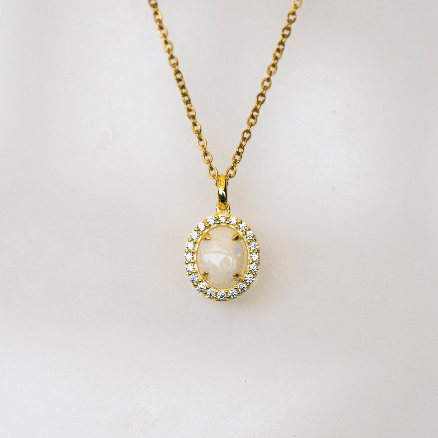 Gold necklace with a pendant featuring a white opal stone on a light gray background