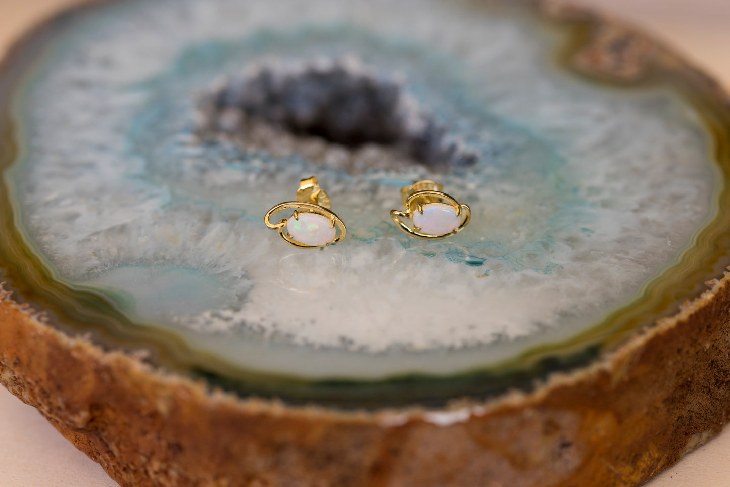 Gold earrings with white opal stones on a geode slice