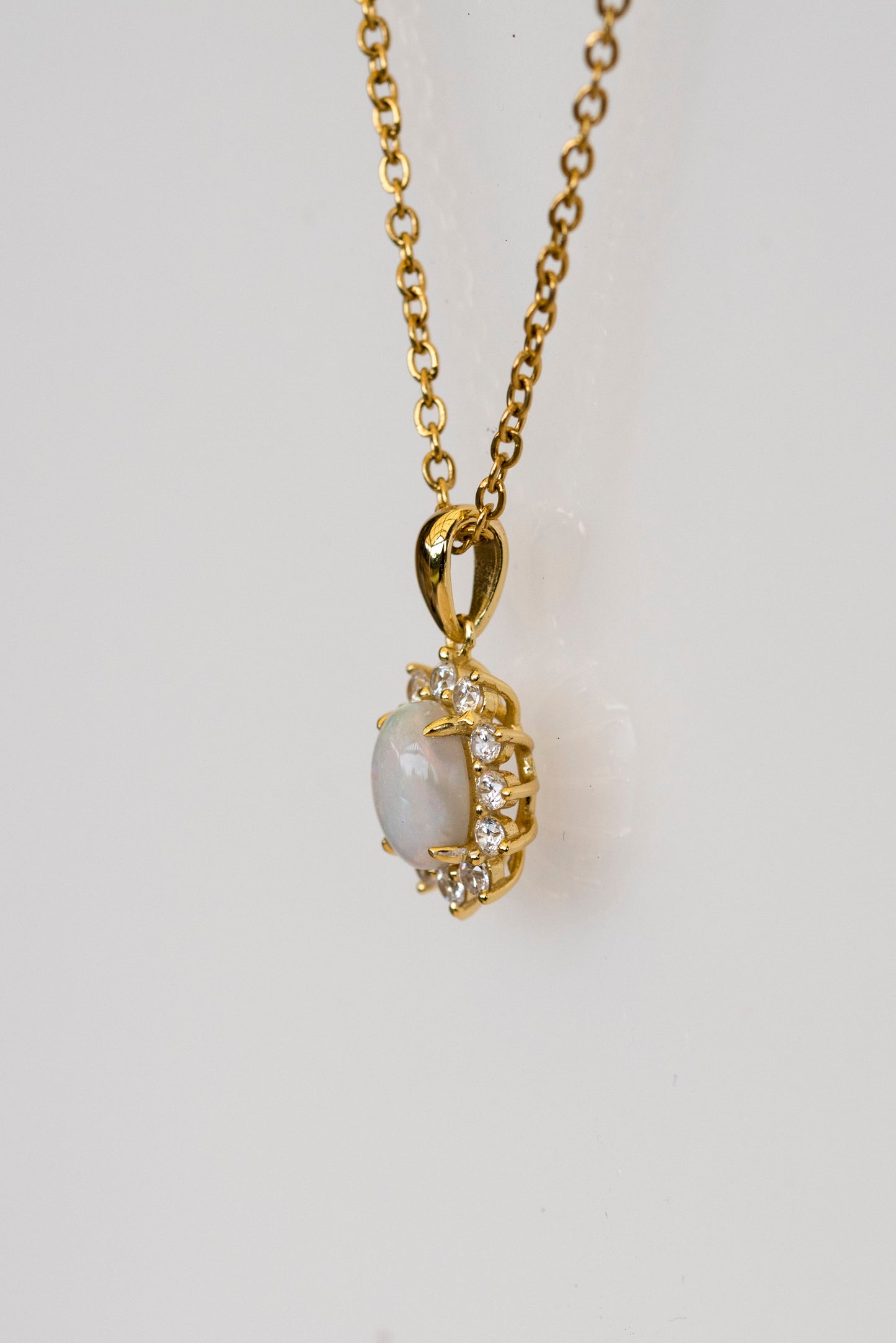Gold necklace with a pendant featuring a central opal stone and smaller stones on a light gray background