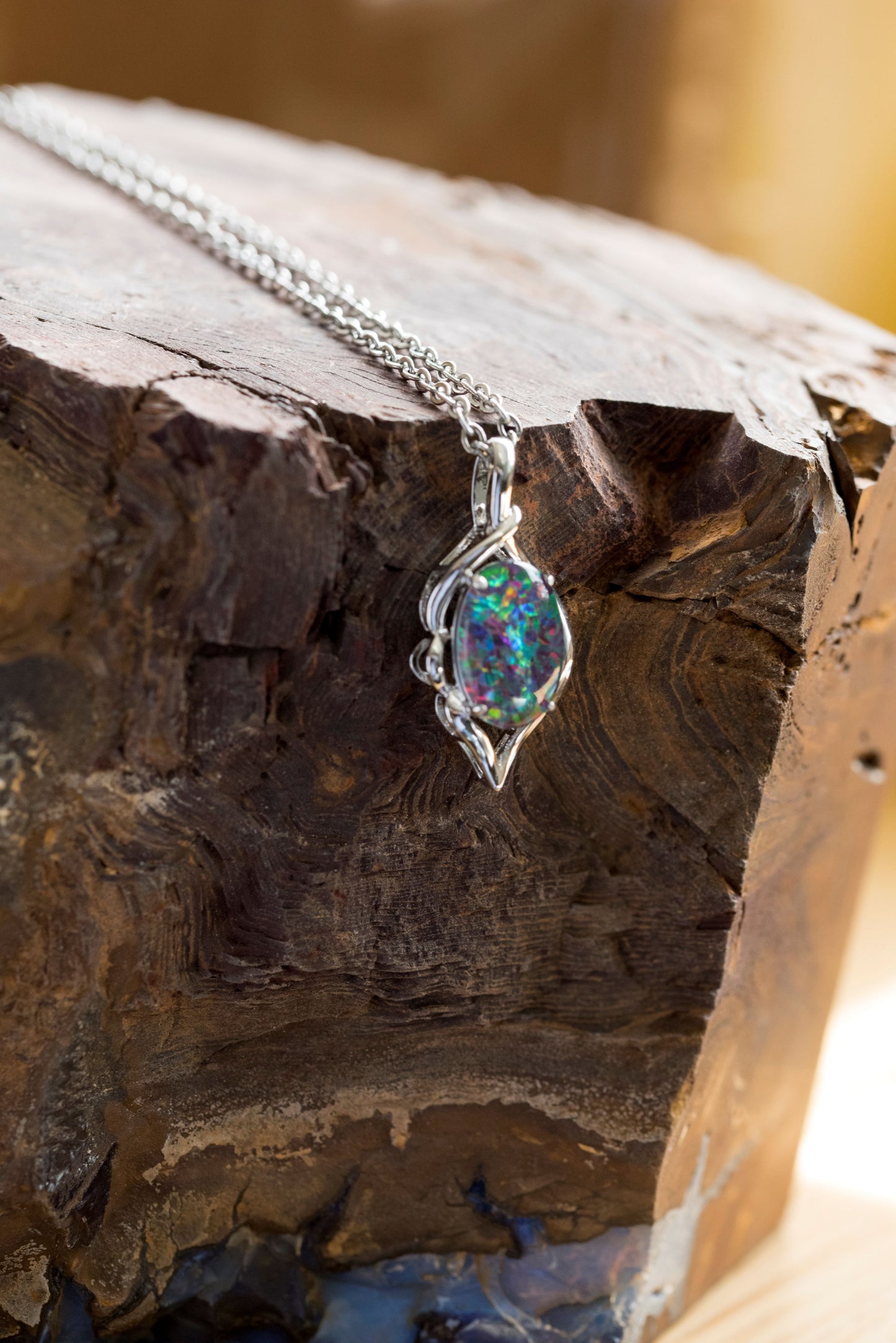 Multicolored opal gemstone pendant on a silver chain against a wooden background