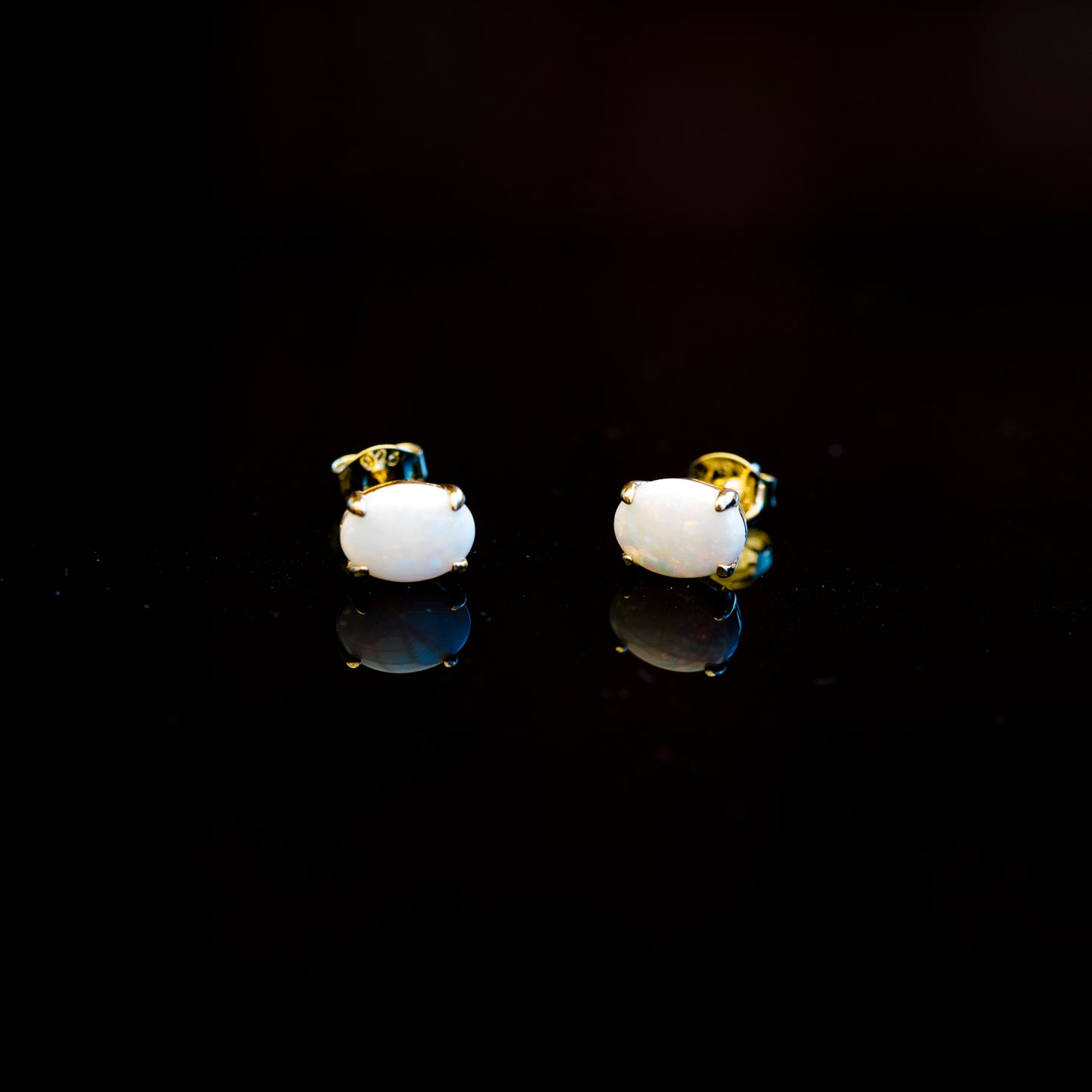 Pair of white earrings with gold accents on a black background