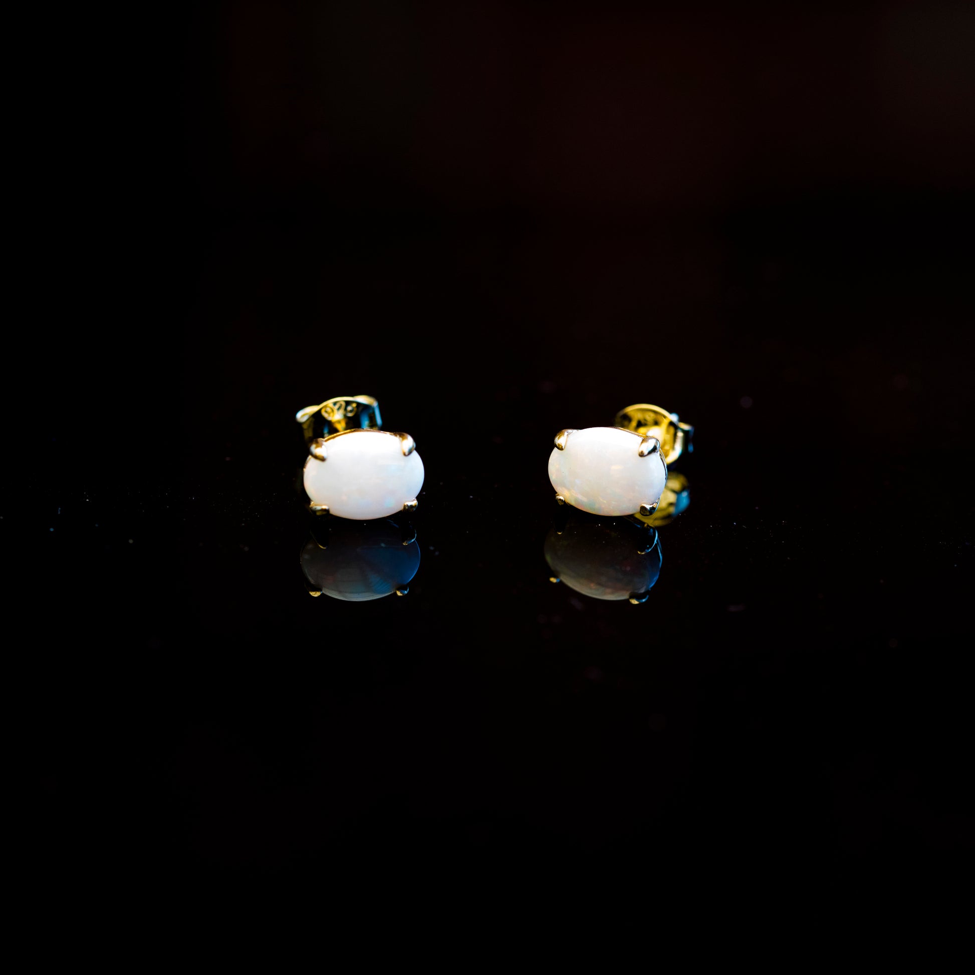 Pair of white earrings with gold accents on a black background