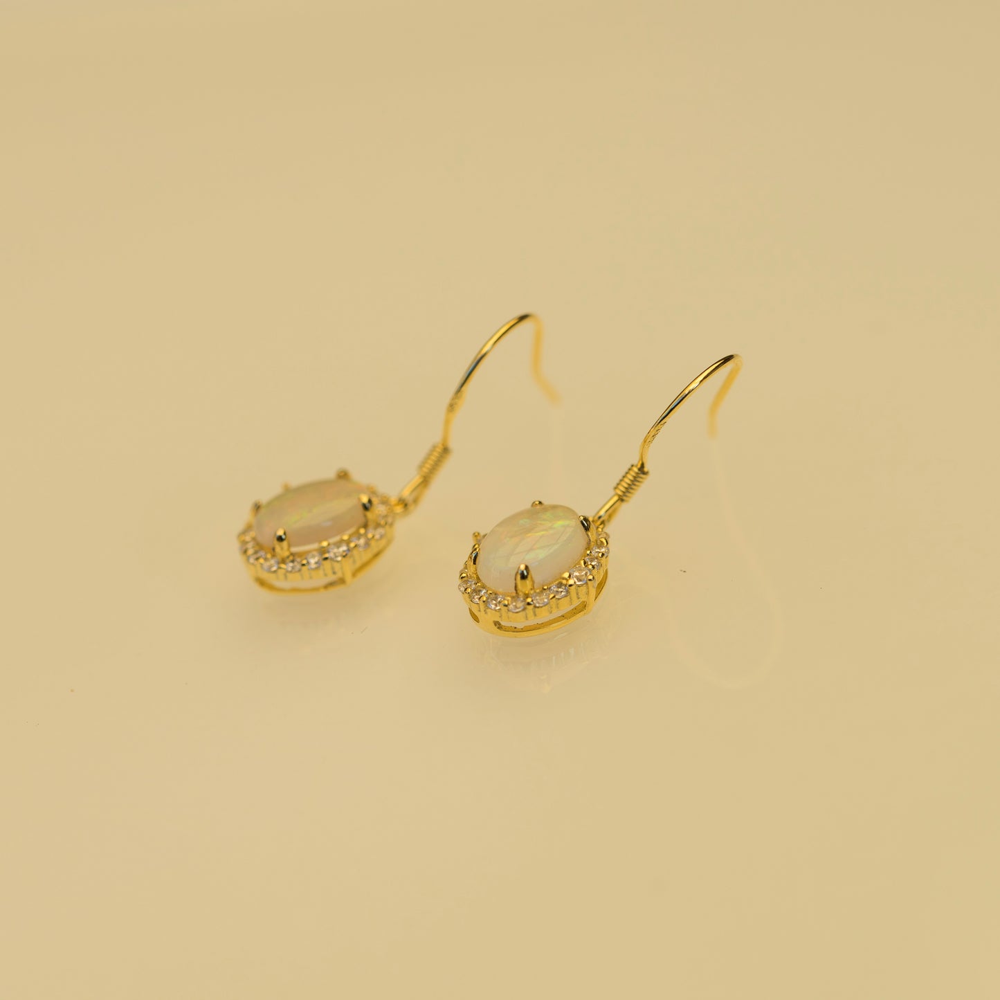 Gold earrings with a central gemstone on a beige background