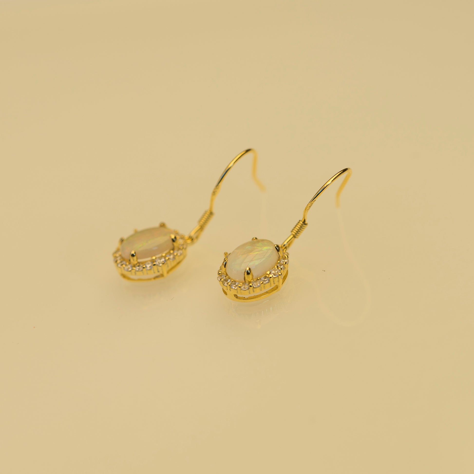 Gold earrings with a central gemstone on a beige background