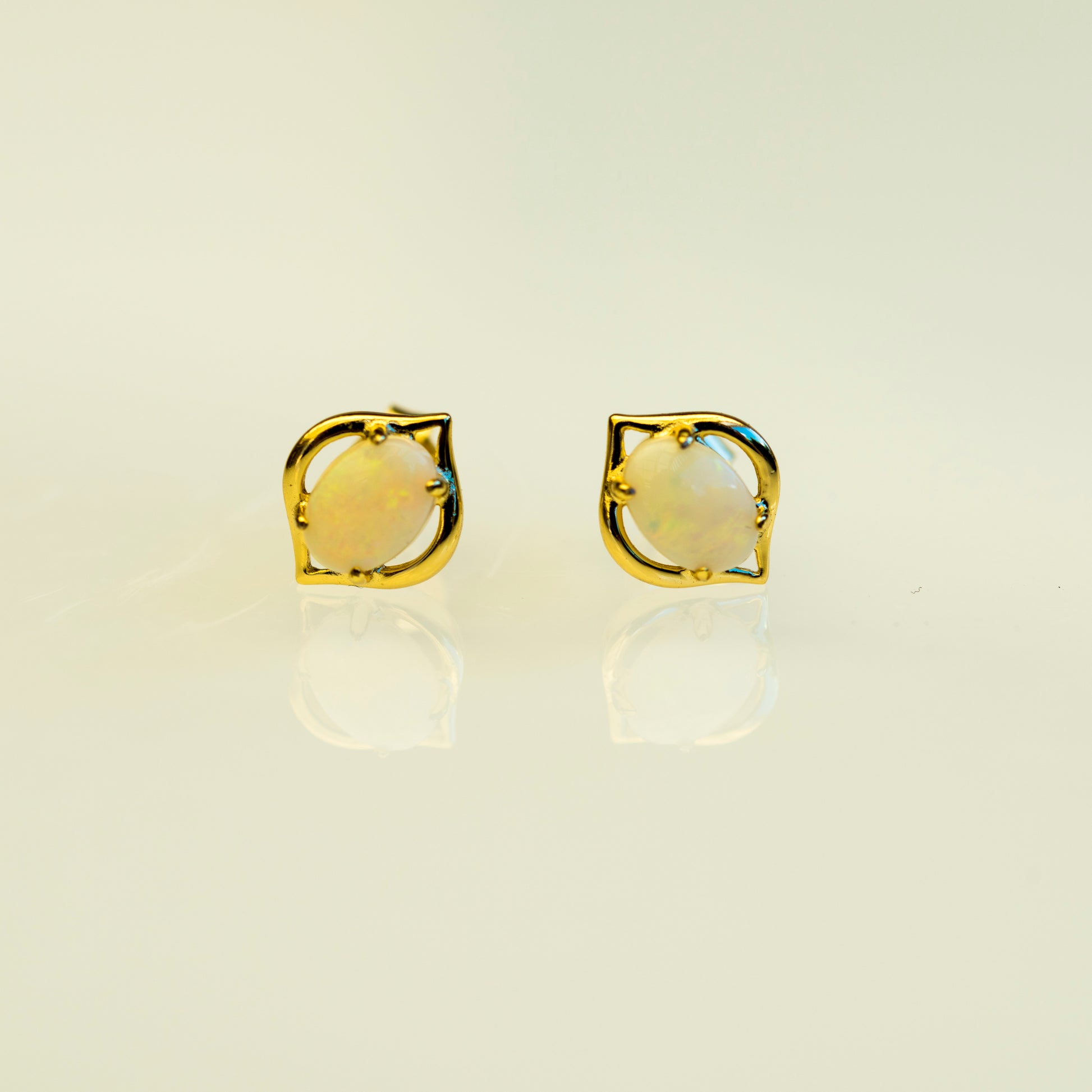 Gold earrings with a yellow opal gemstone on a beige background