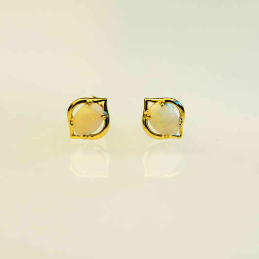 Gold earrings with a yellow opal gemstone on a beige background