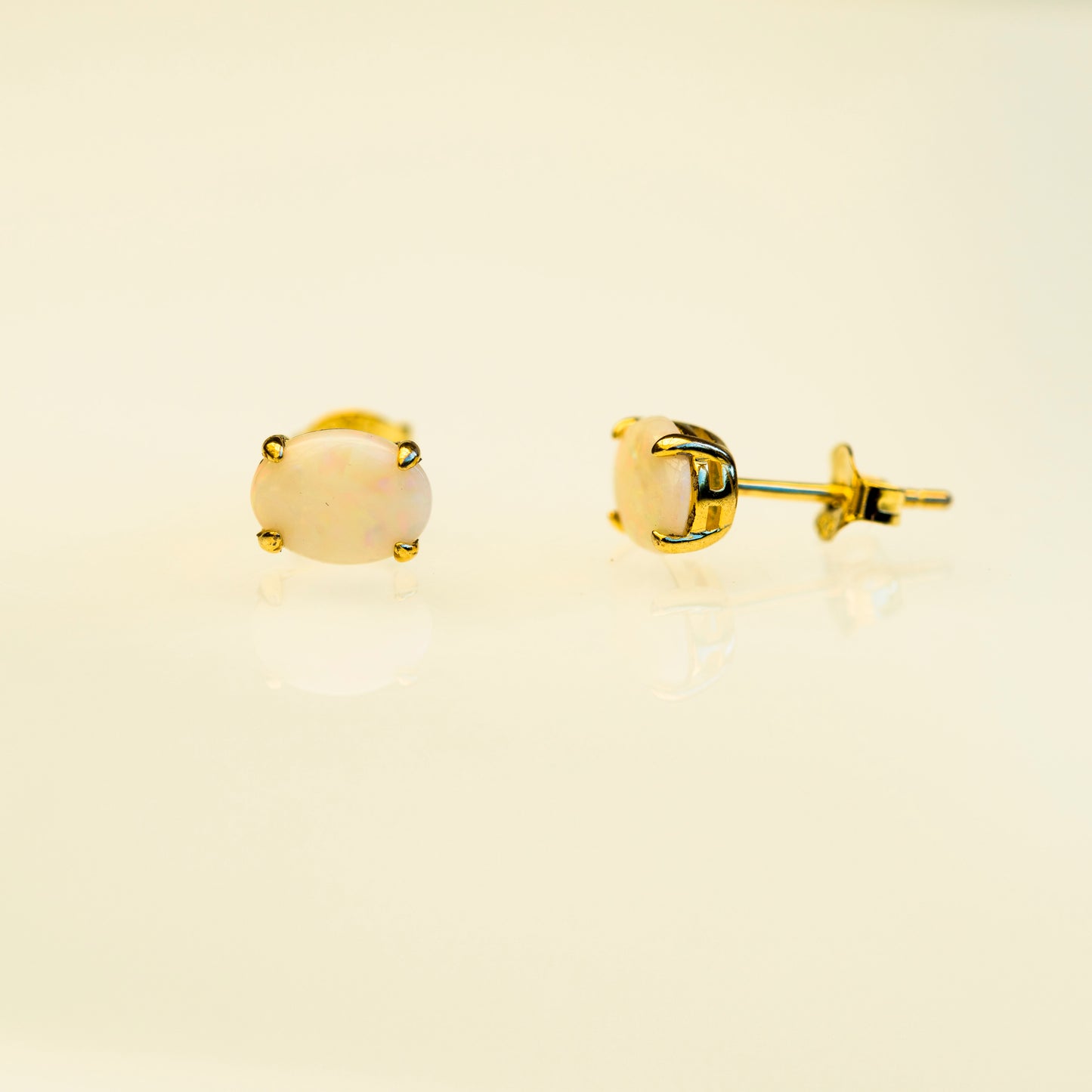Gold stud earrings with a beige stone on a beige background