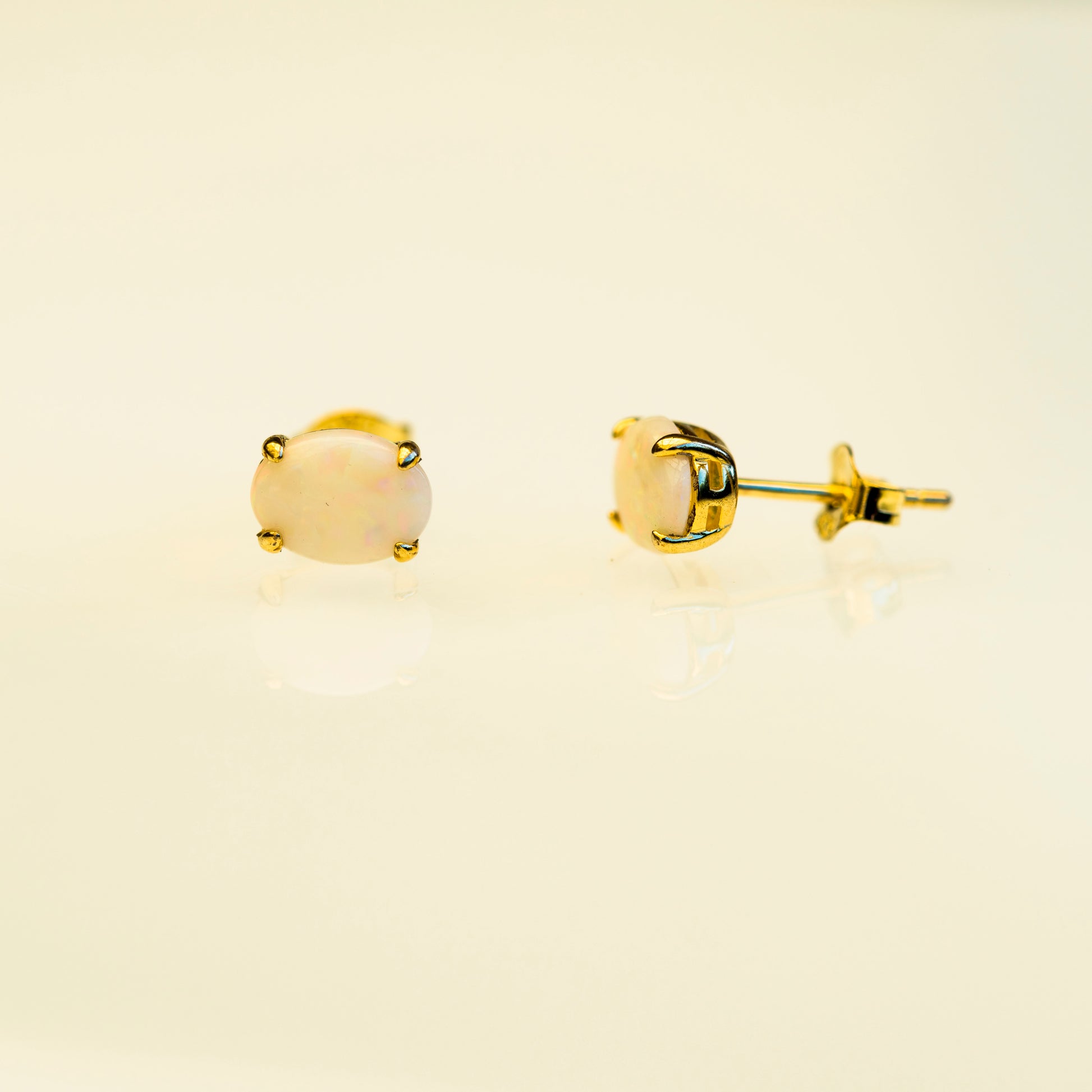 Gold stud earrings with a beige stone on a beige background
