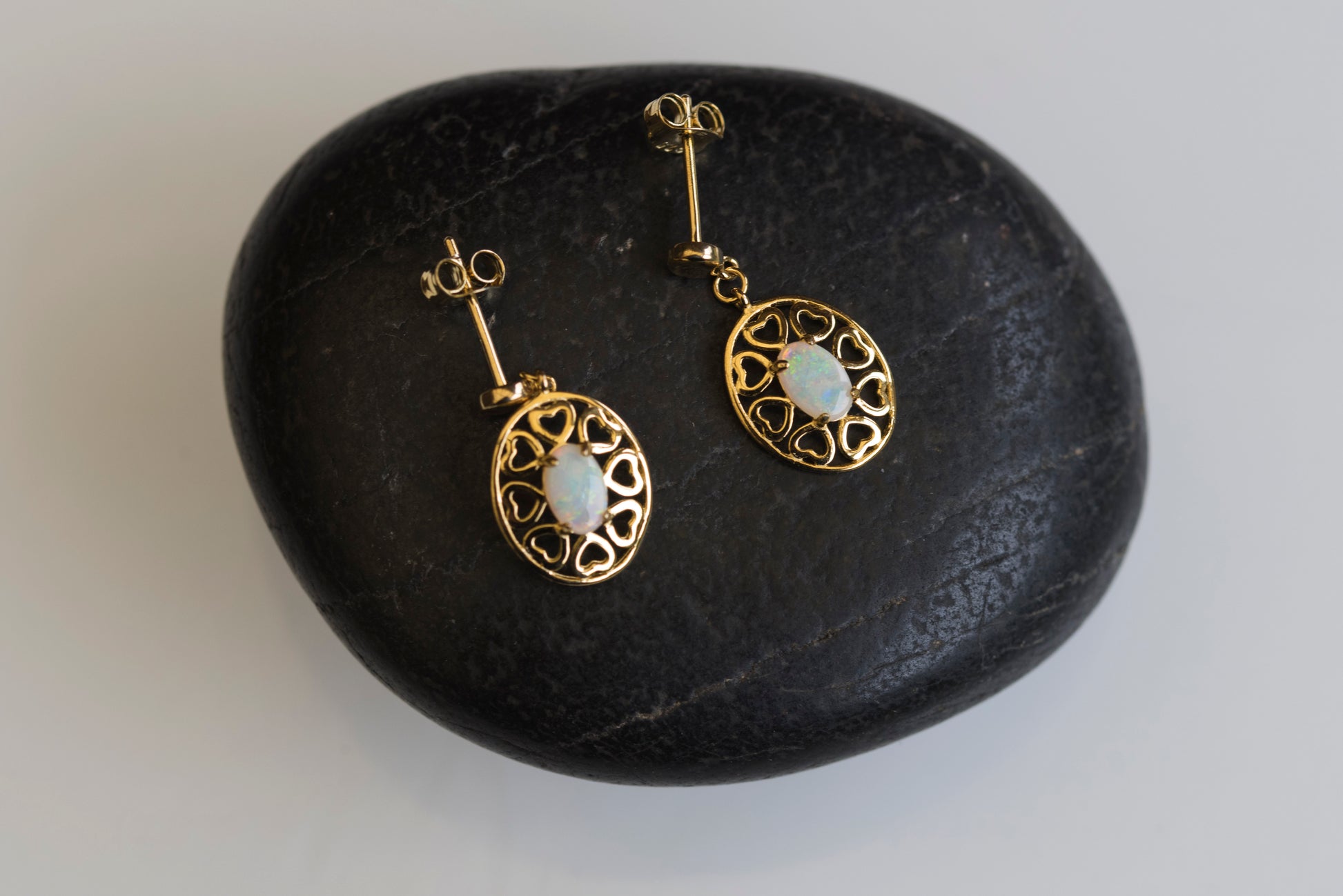 Gold earrings with opal stones on a dark stone surface