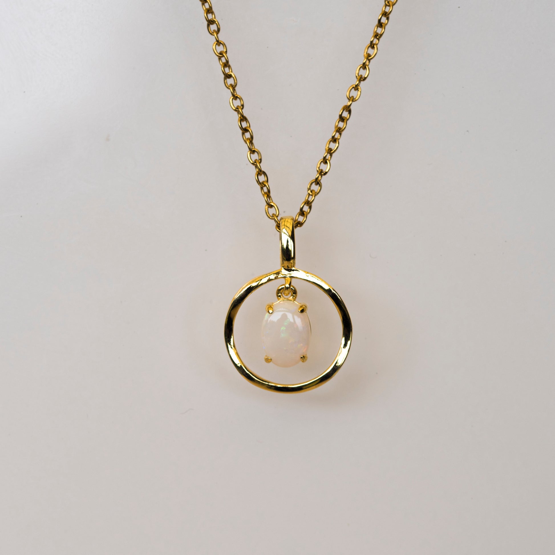 Gold necklace with a pendant featuring an opal on a light gray background