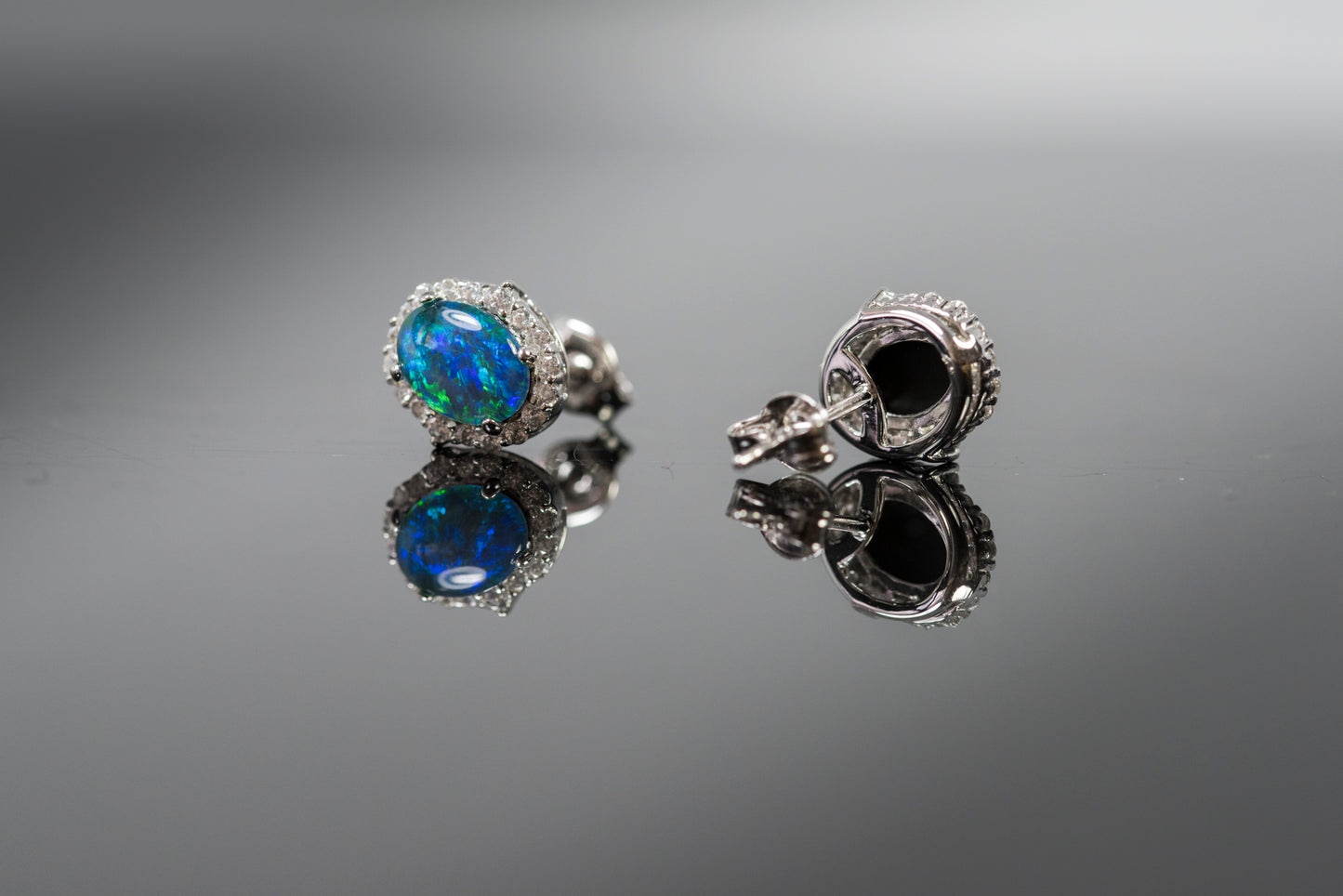Pair of silver earrings with opal gemstones on a reflective surface