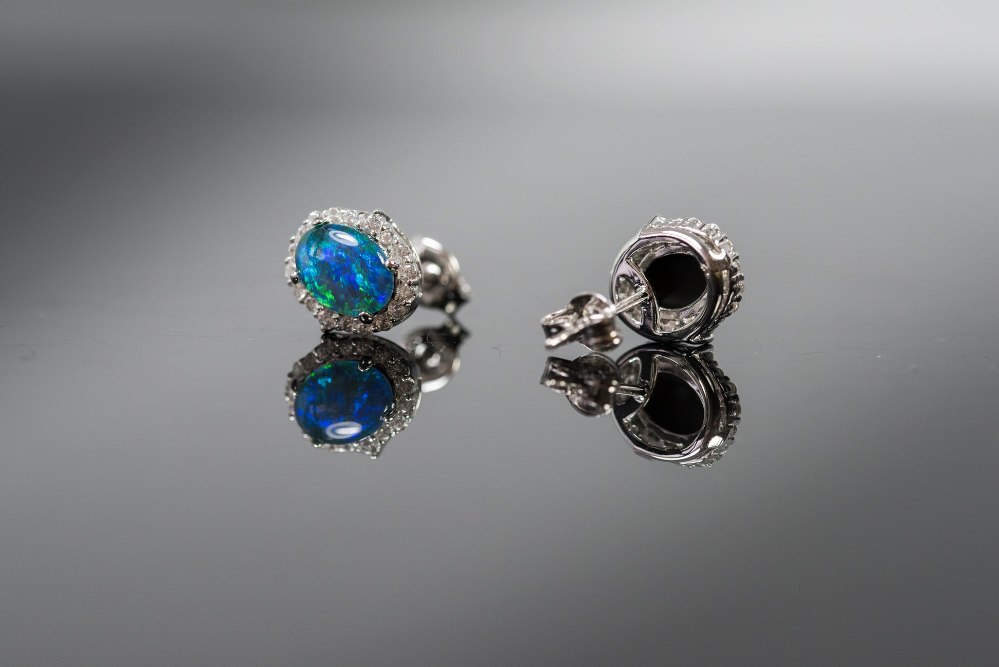 Pair of silver earrings with opal gemstones on a reflective surface