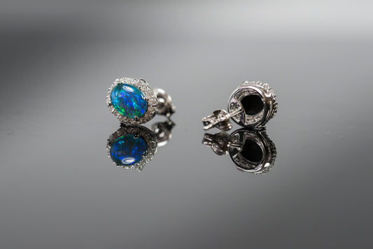 Pair of silver earrings with opal gemstones on a reflective surface