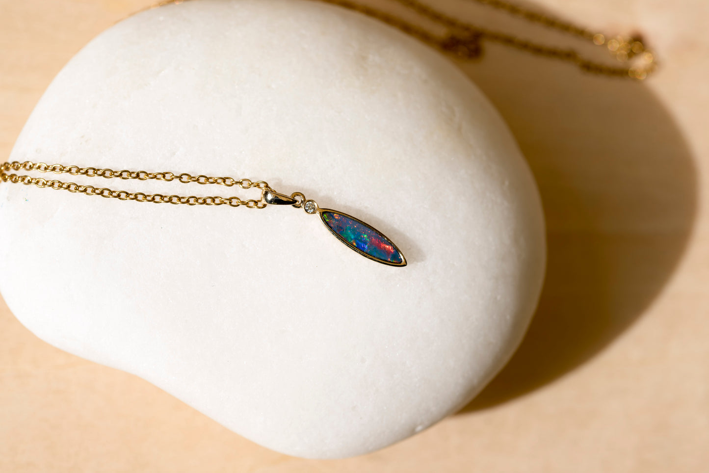 Necklace with a colorful opal pendant on a white stand against a beige background