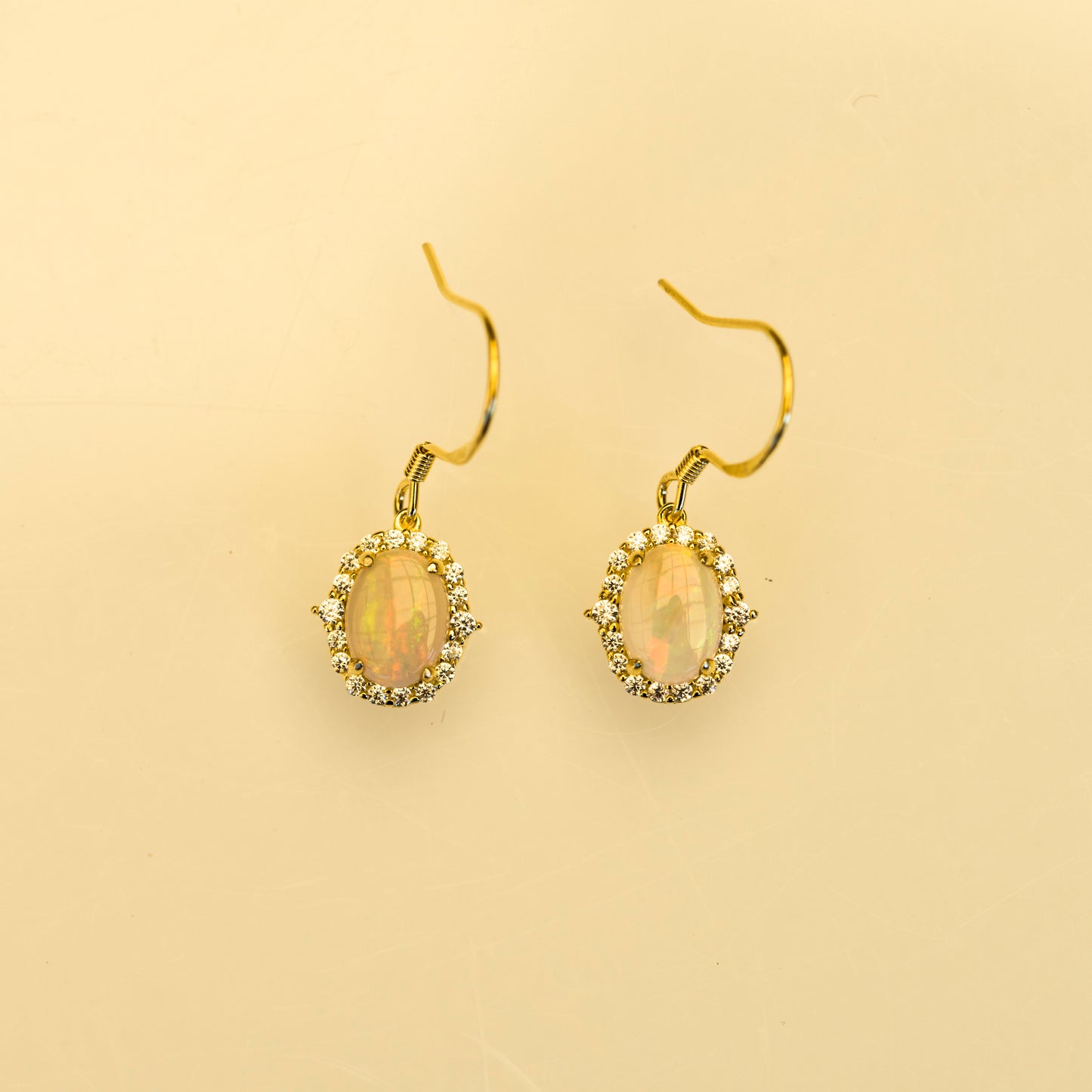Gold earrings with opal stones on a beige background