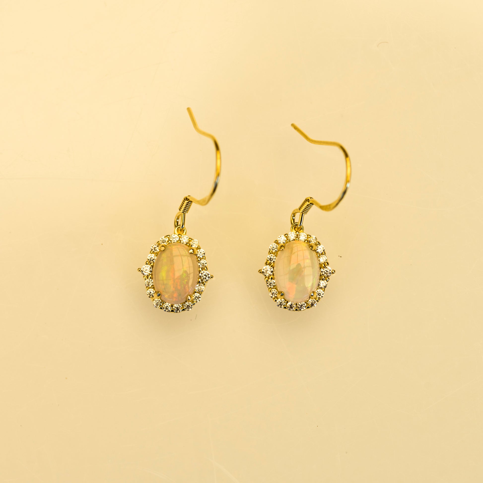 Gold earrings with opal stones on a beige background