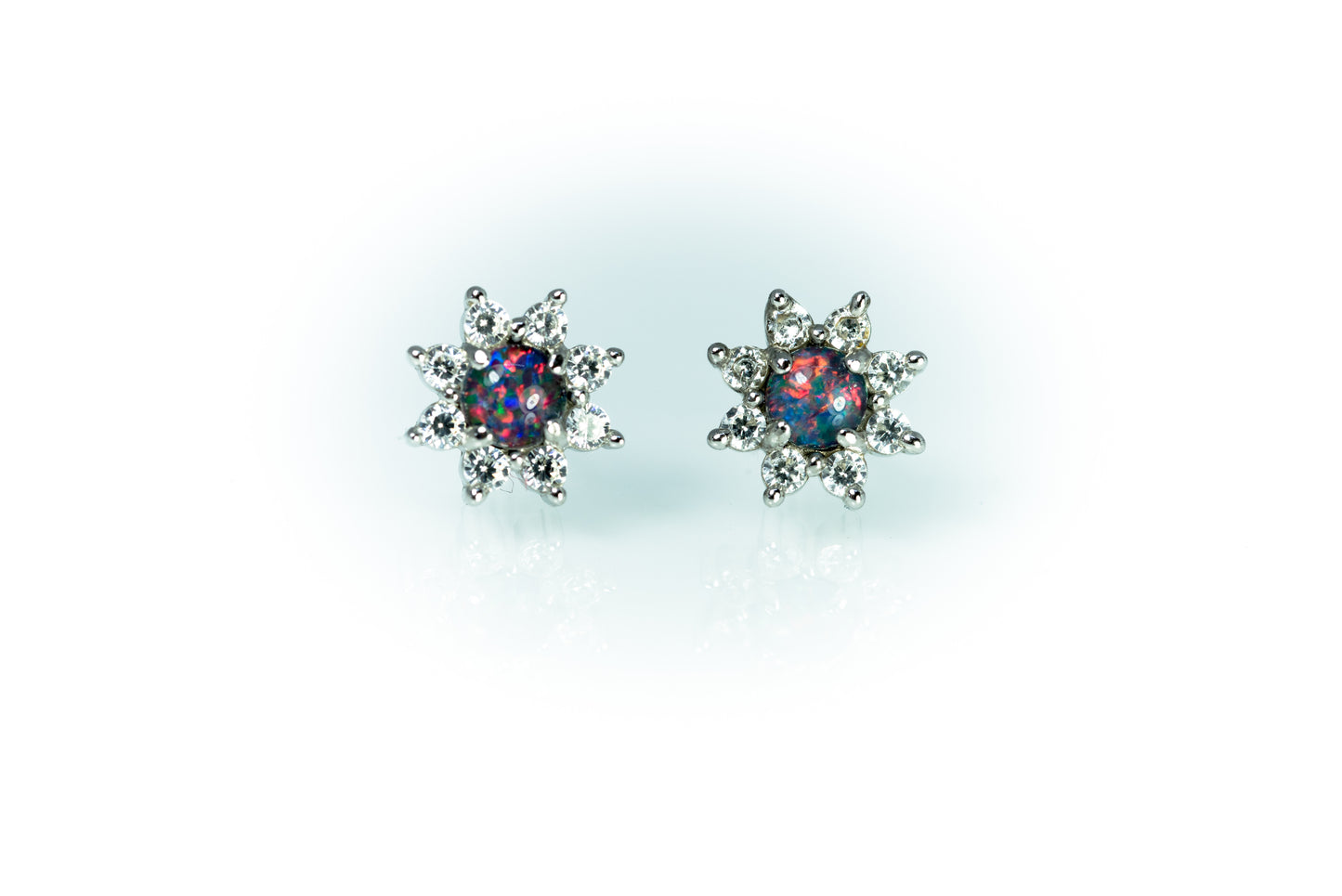 Pair of star-shaped earrings with colorful opal gemstones on a light blue background