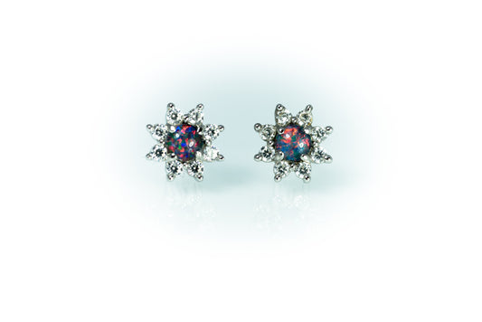 Pair of star-shaped earrings with colorful opal gemstones on a light blue background