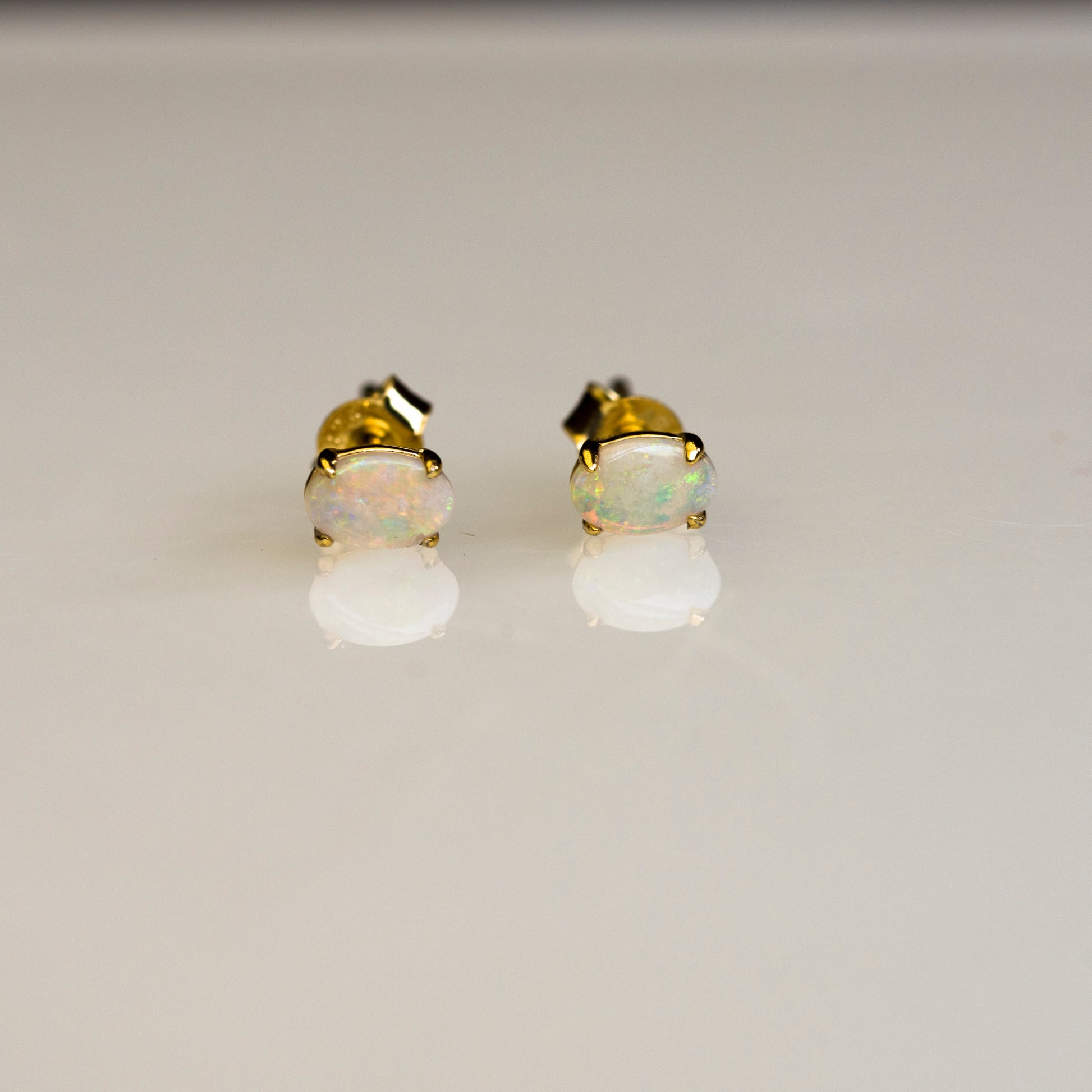 Pair of gold and opal stud earrings on a light gray background