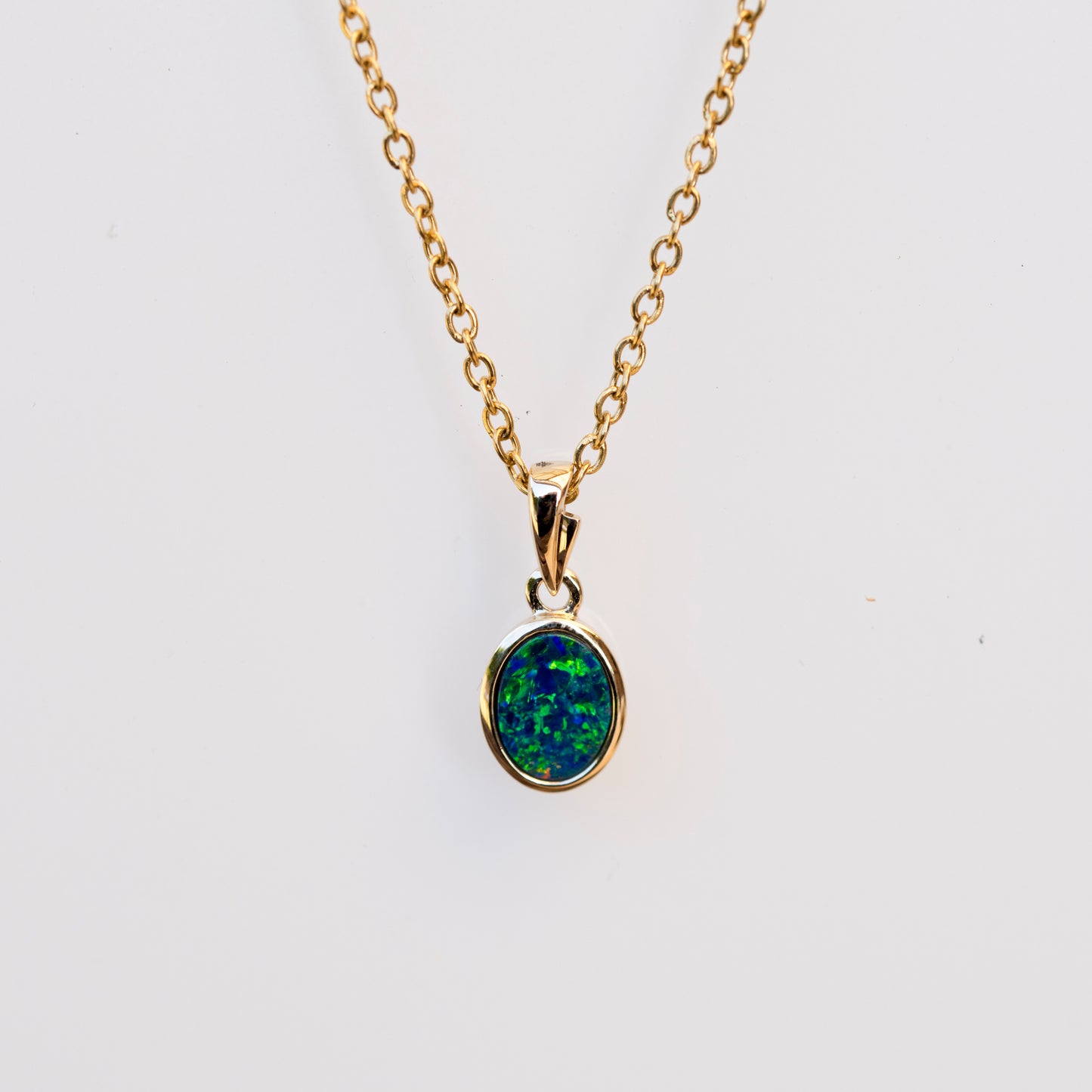 Gold necklace with a green opal pendant on a white background