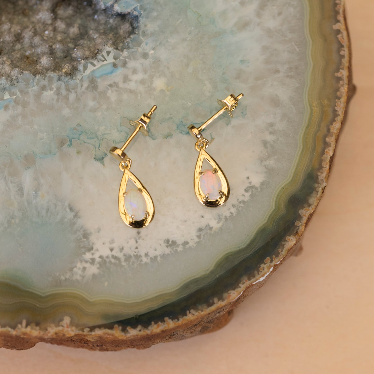 Gold teardrop opal earrings on a natural stone surface