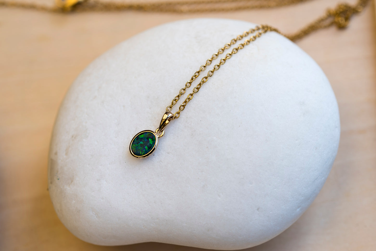 Gold necklace with a green opal gemstone pendant on a white stone