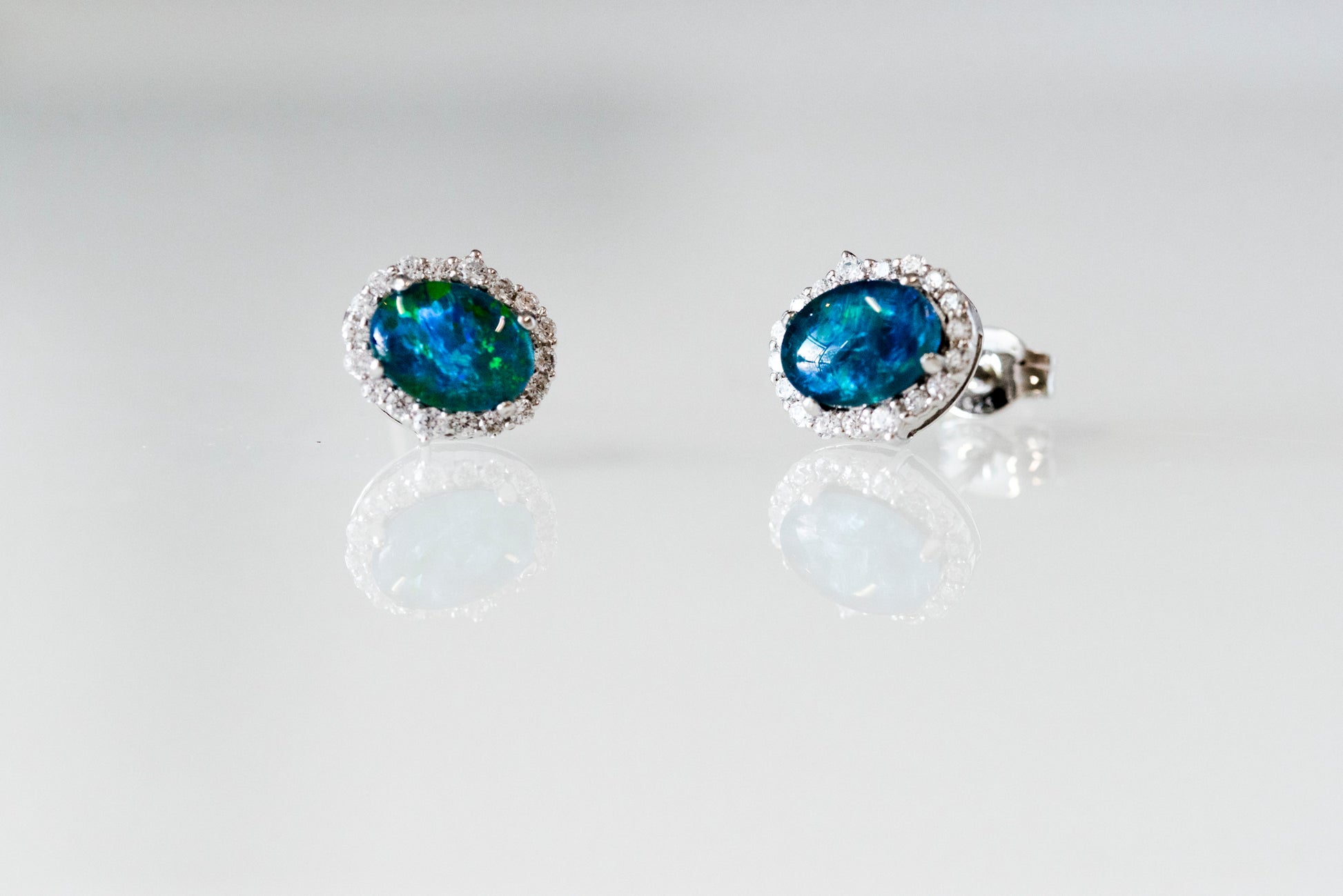 Pair of opal earrings on a reflective surface