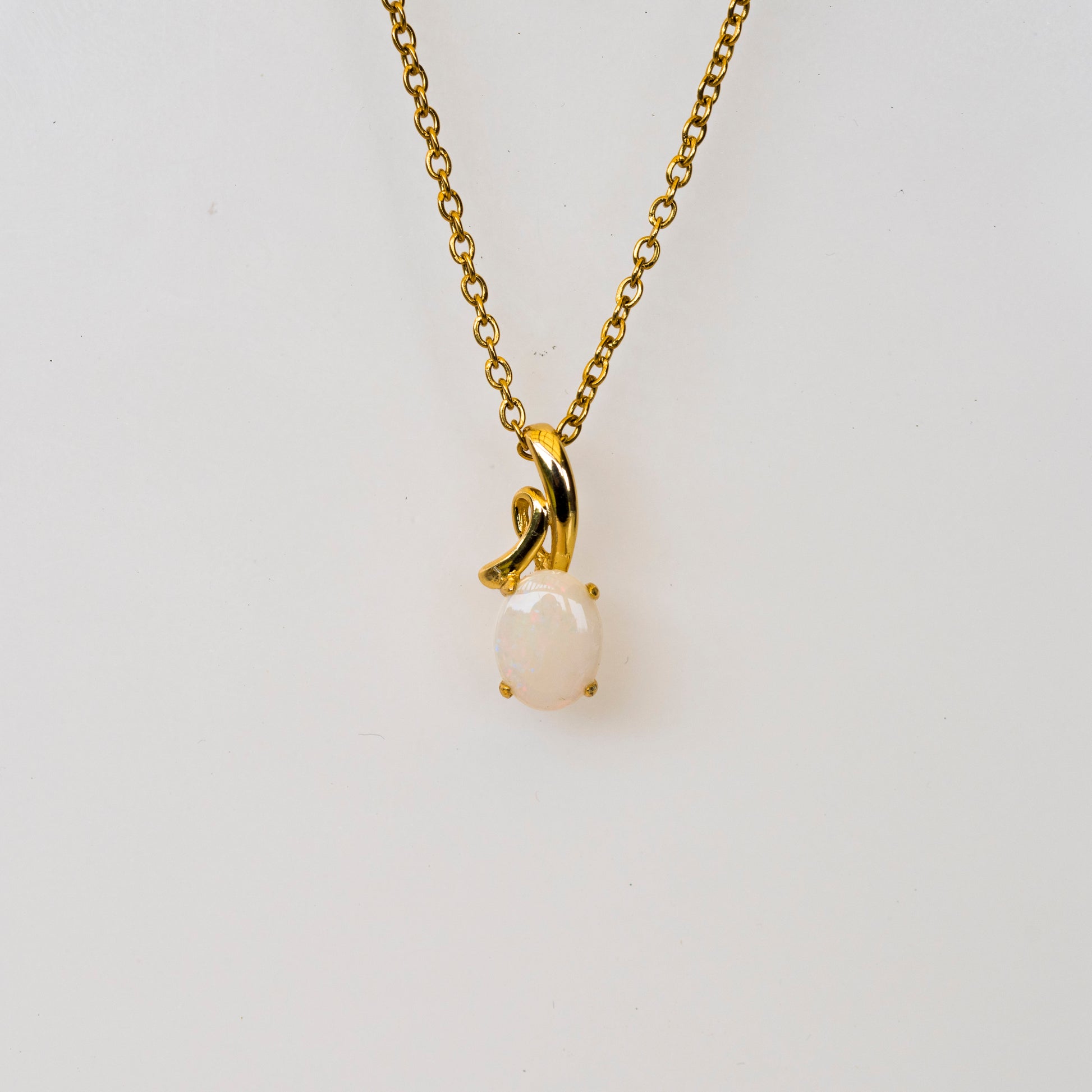 Gold necklace with a natural opal pendant on a light gray background