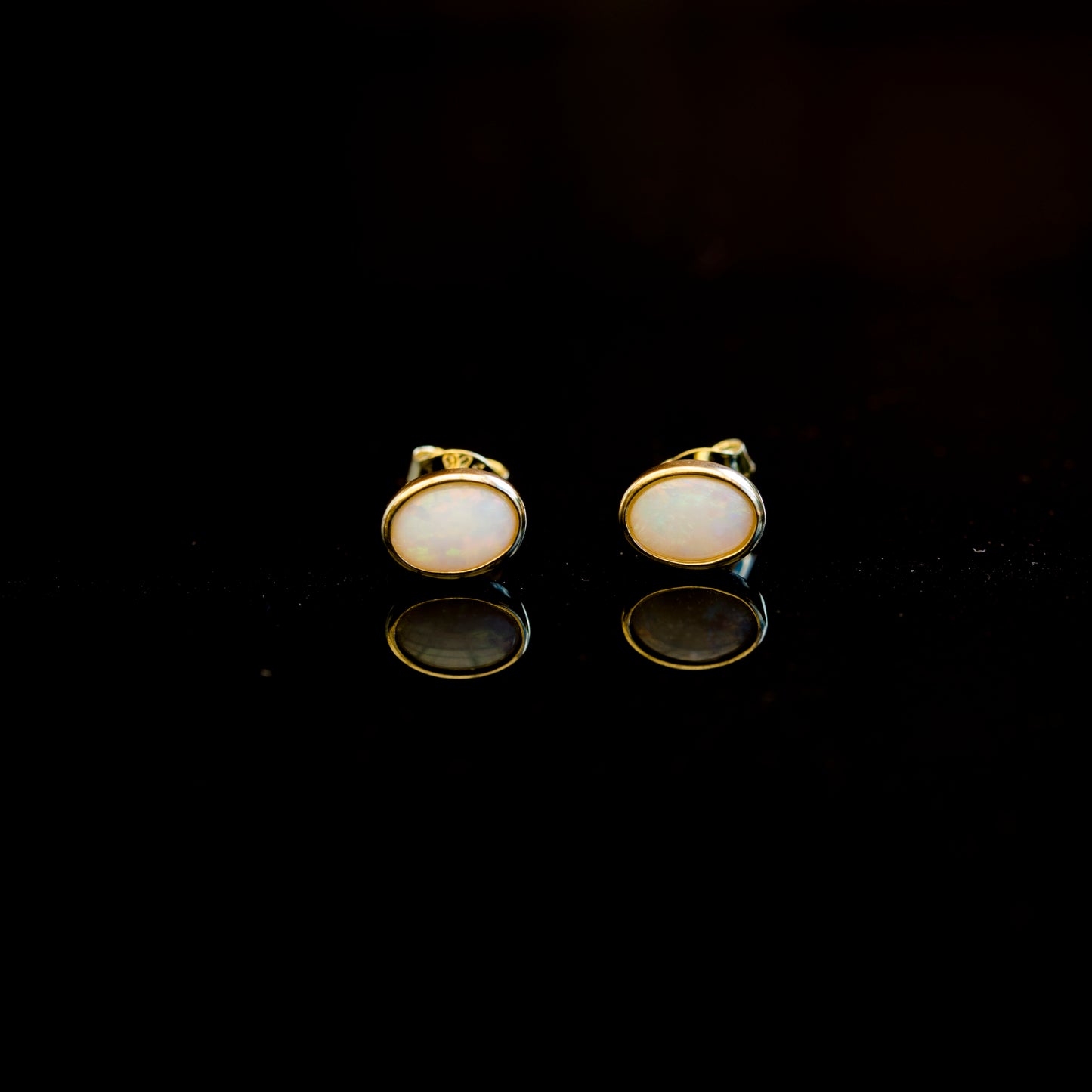 Pair of gold earrings with natural opal stones on a black background