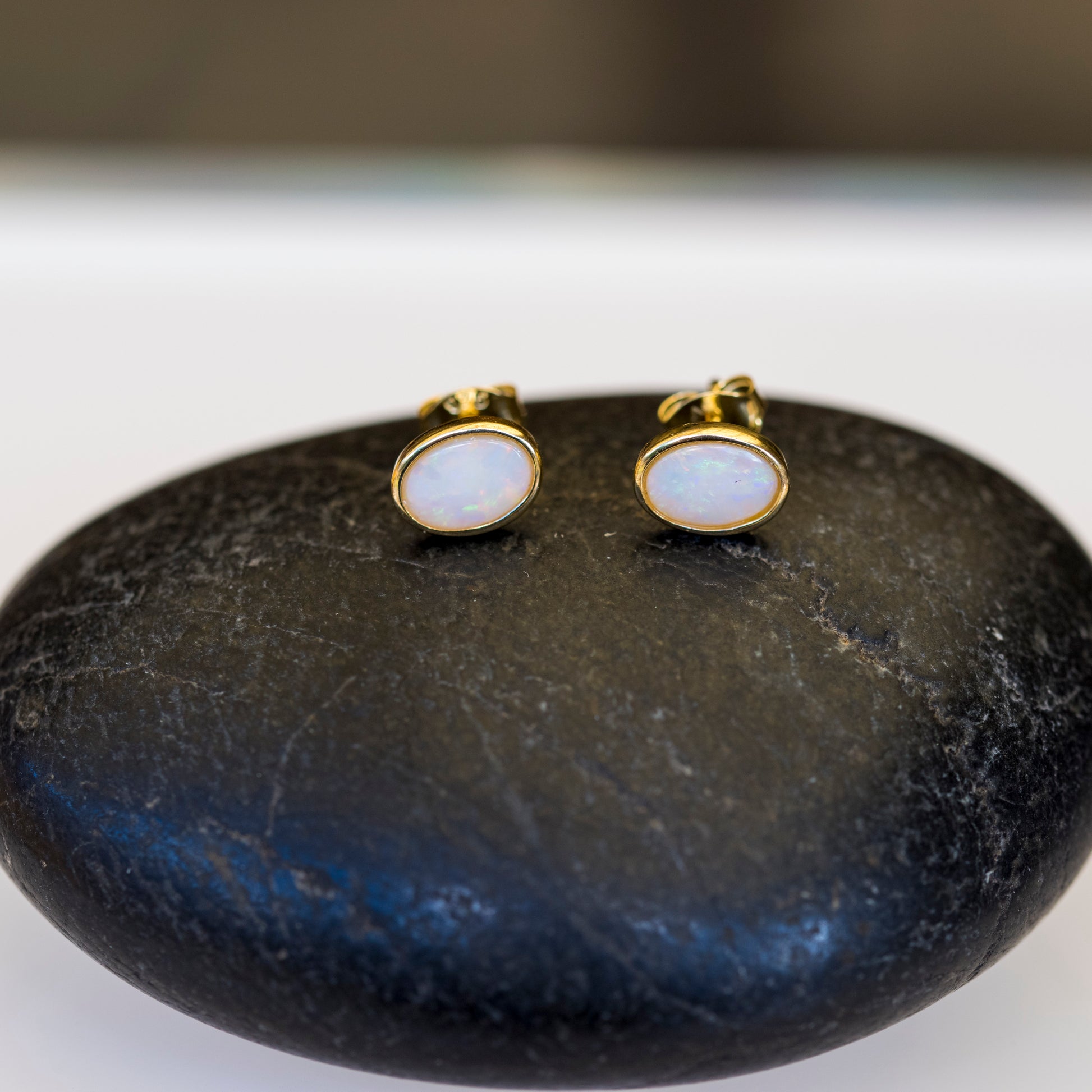 Pair of gold earrings with white opal stones on a dark stone surface