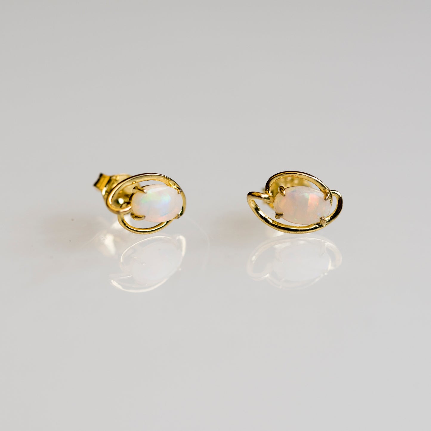 Gold earrings with opal stones on a light gray background