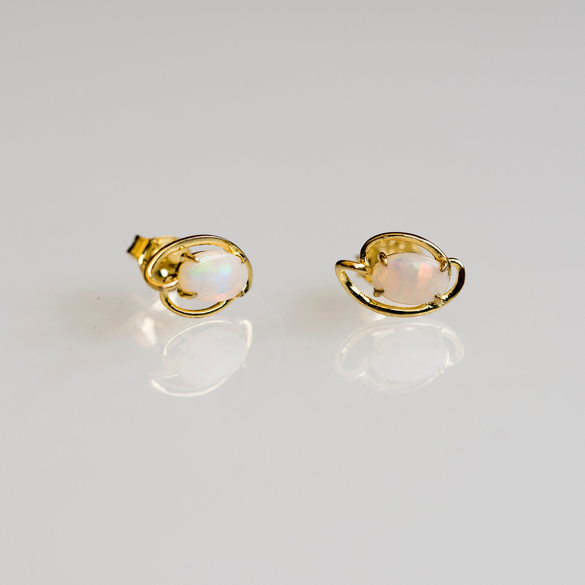Gold earrings with opal stones on a light gray background
