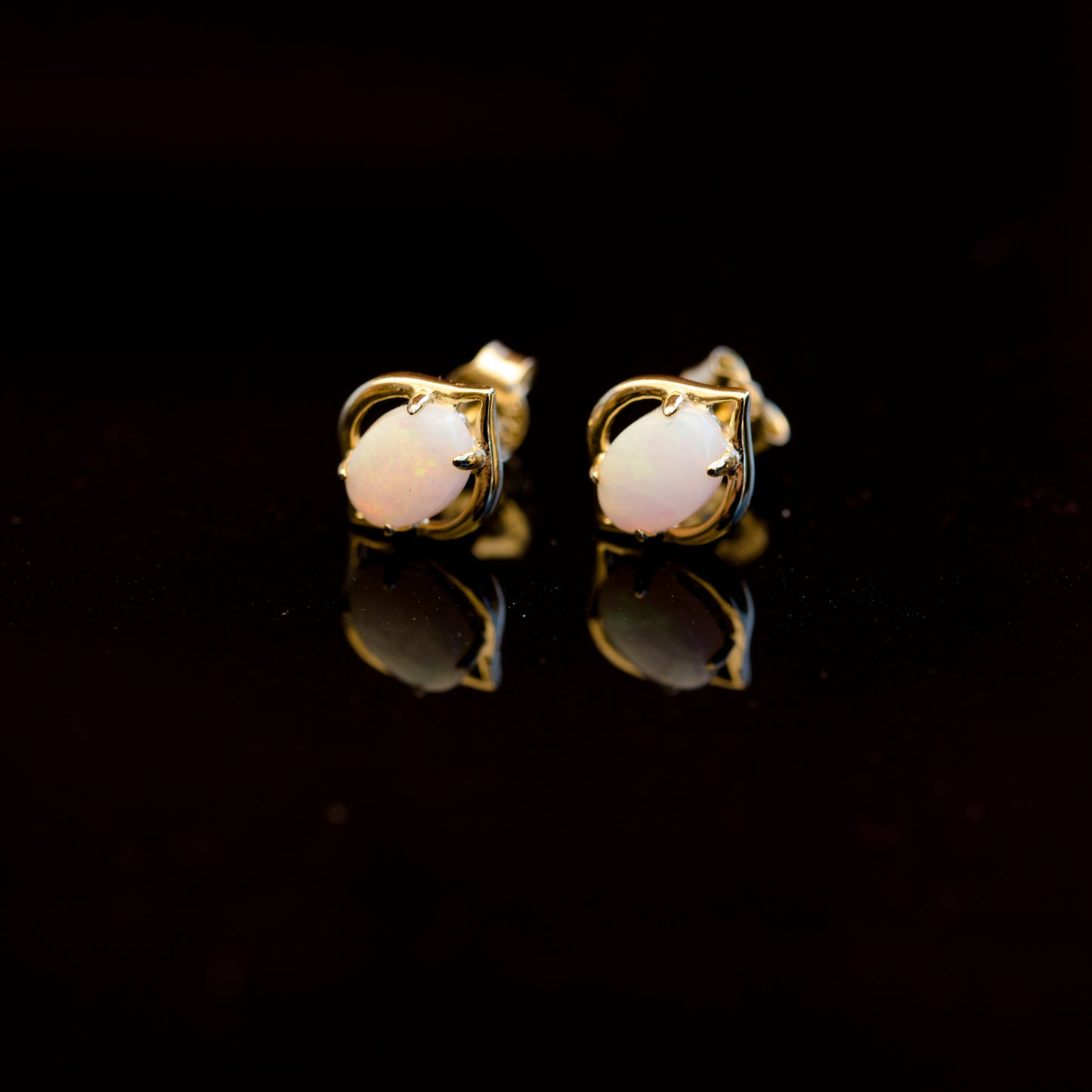 Pair of gold opal earrings with white gemstones on a black background