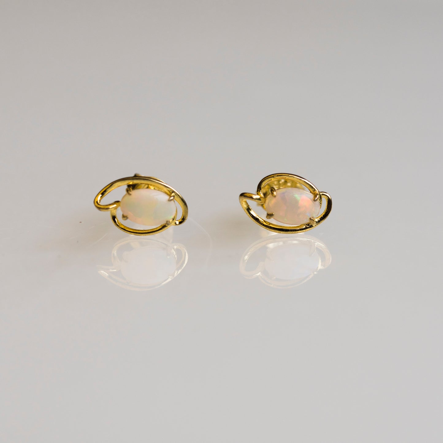 Pair of gold earrings with opal stones on a light gray background