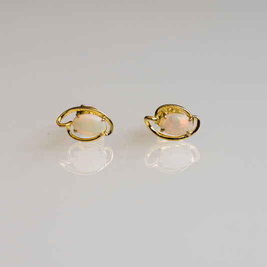 Pair of gold earrings with opal stones on a light gray background