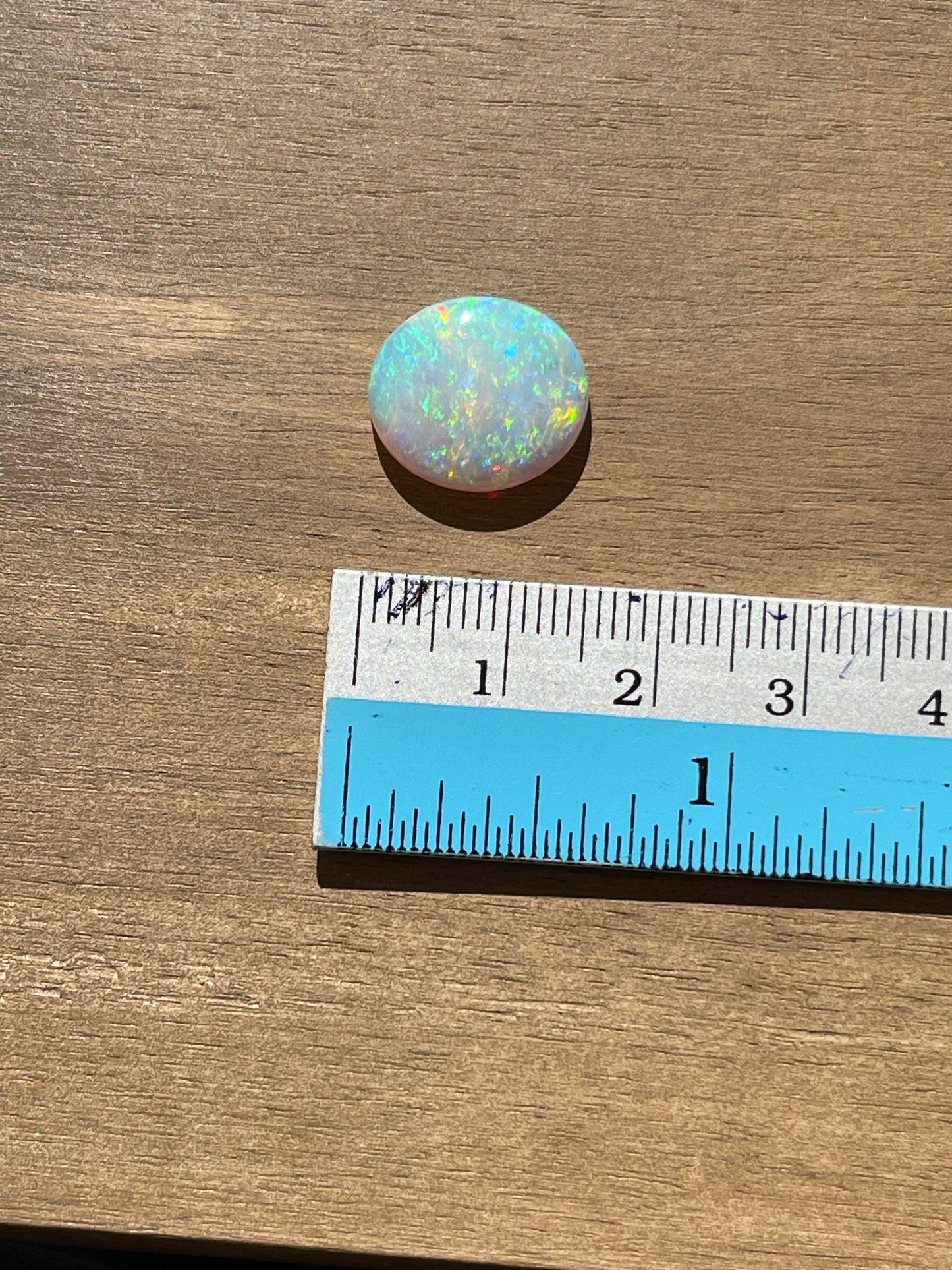 Opal stone next to a ruler on a wooden surface