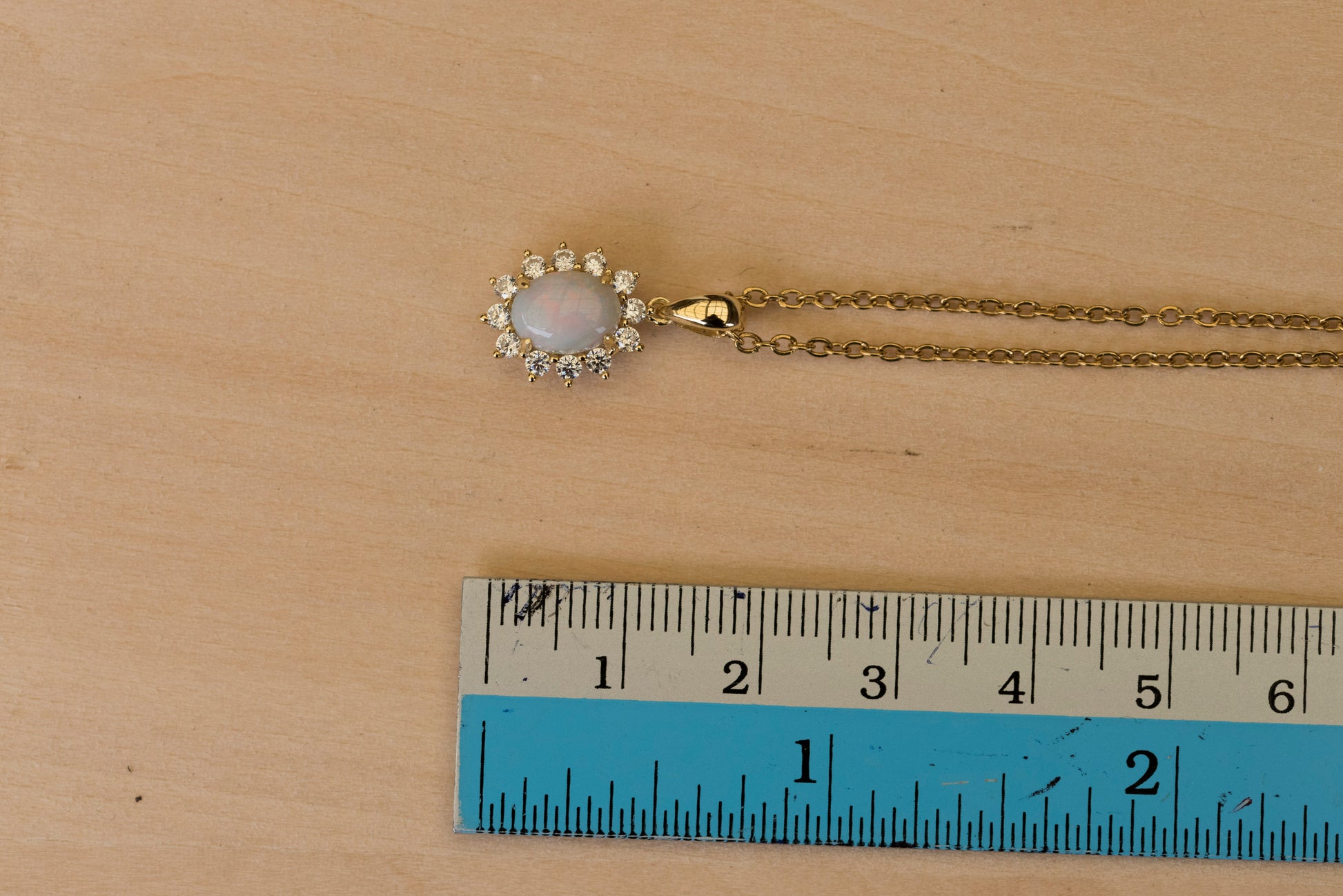 Gold opal necklace with a pendant on a wooden surface, measured by a ruler.