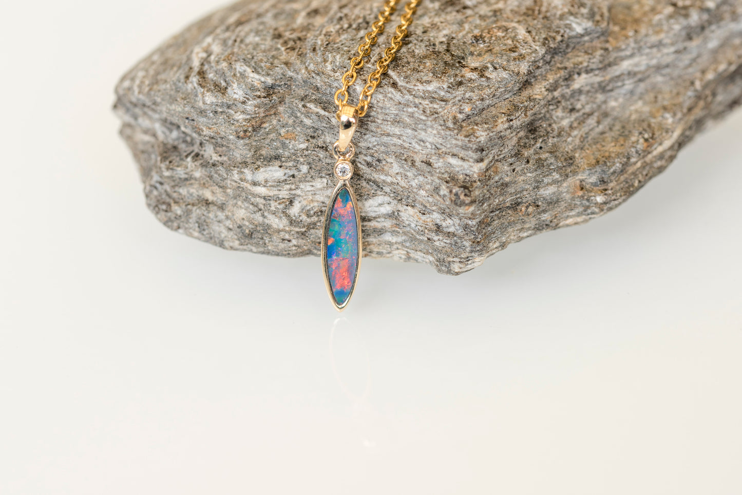 Opal pendant necklace on a gold chain against a stone background