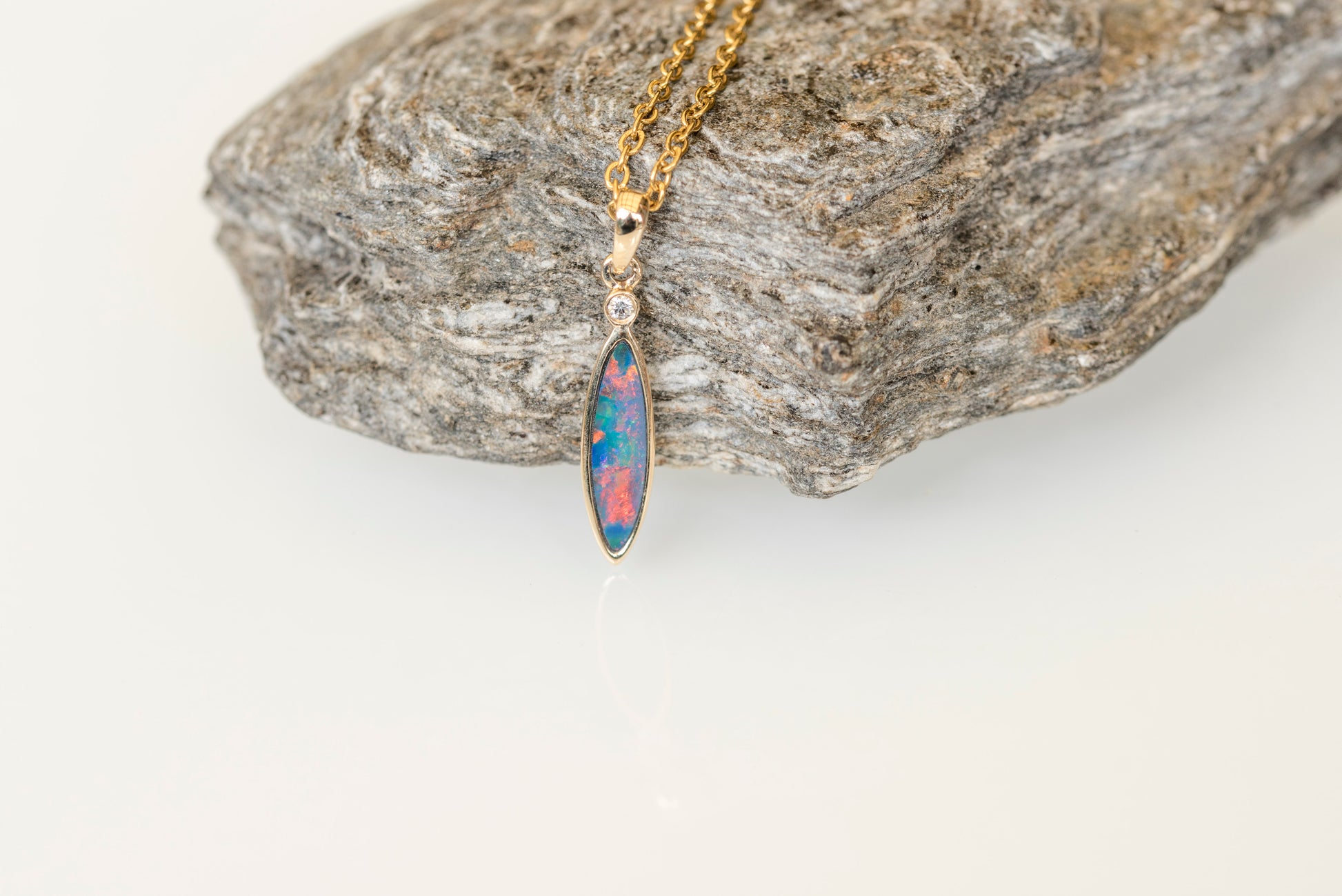 Opal pendant necklace on a gold chain against a stone background