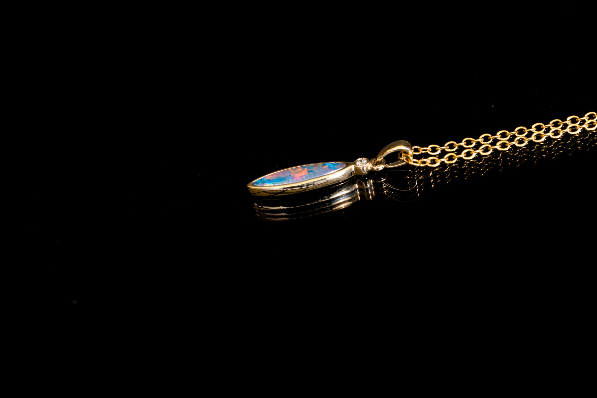 Gold chain with a small opal pendant on a black background
