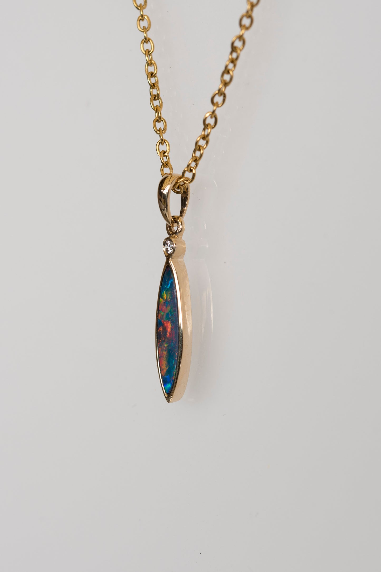 Gold opal necklace with a colorful pendant on a light gray background