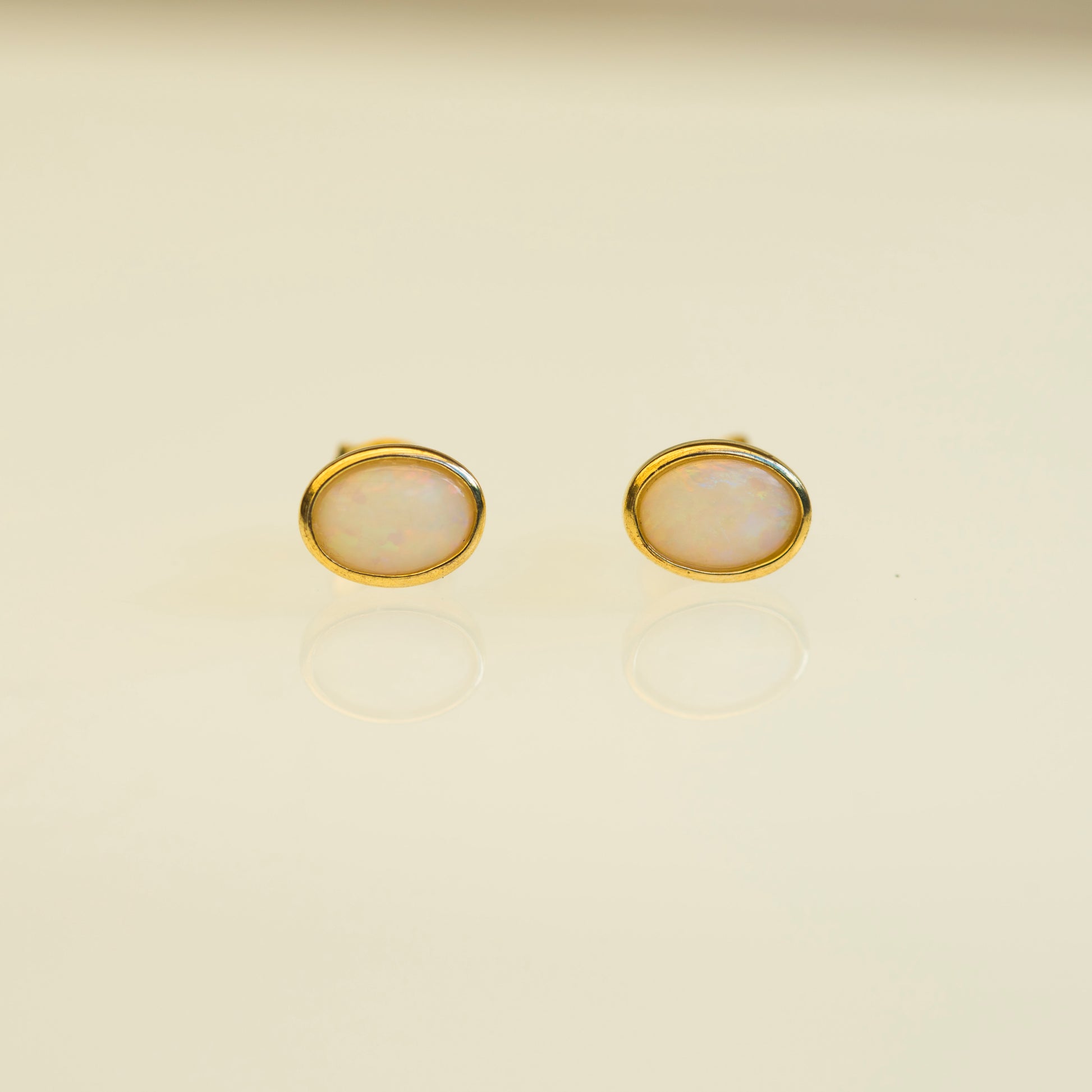 Pair of gold earrings with round natural opal on a beige background